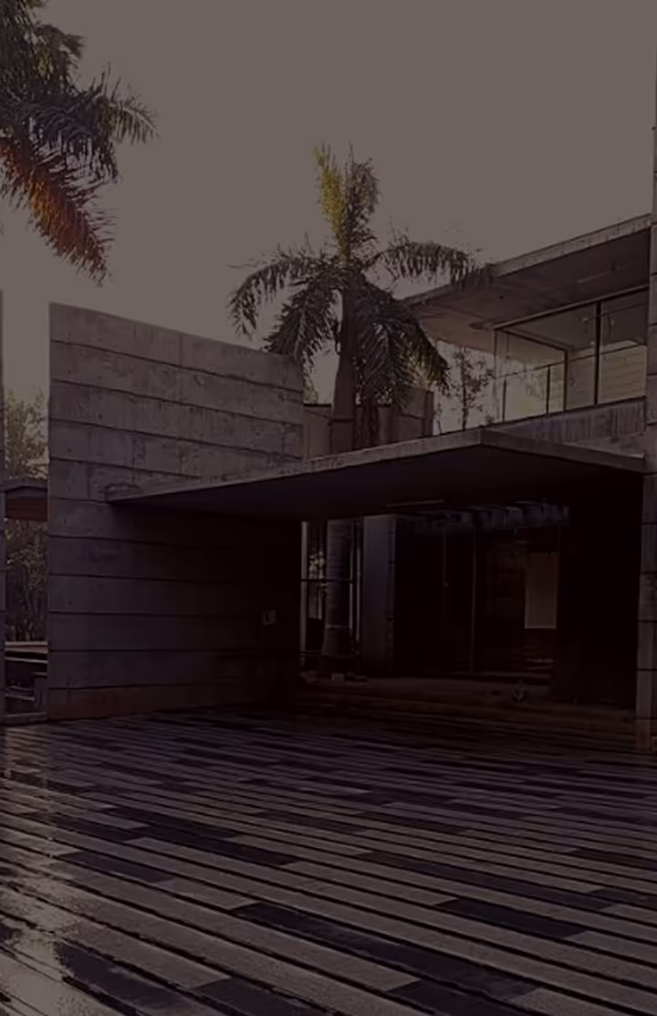 Modern concrete house entrance with large overhang and palm trees in the background.
