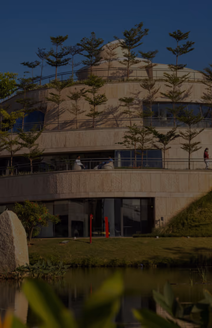 Modern circular building with multiple levels featuring young trees on terraces and a reflecting pond in the foreground.