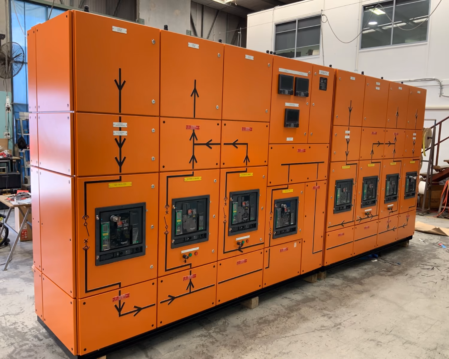 Large orange electrical switchboard with multiple circuit breakers and wiring diagrams in an industrial setting.