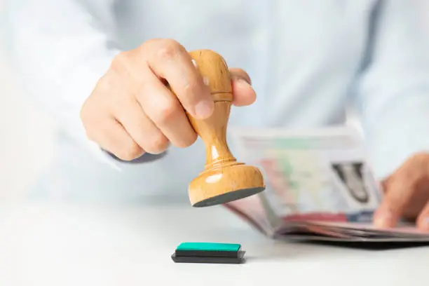 Hand stamping document beside open passport Beyond Border