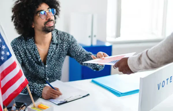 Person handing paper ballot at voting desk Beyond Border