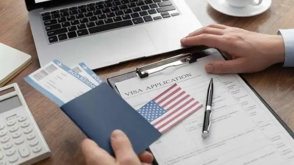 A person holding a passport and boarding pass next to a visa application form and a laptop Beyond Border