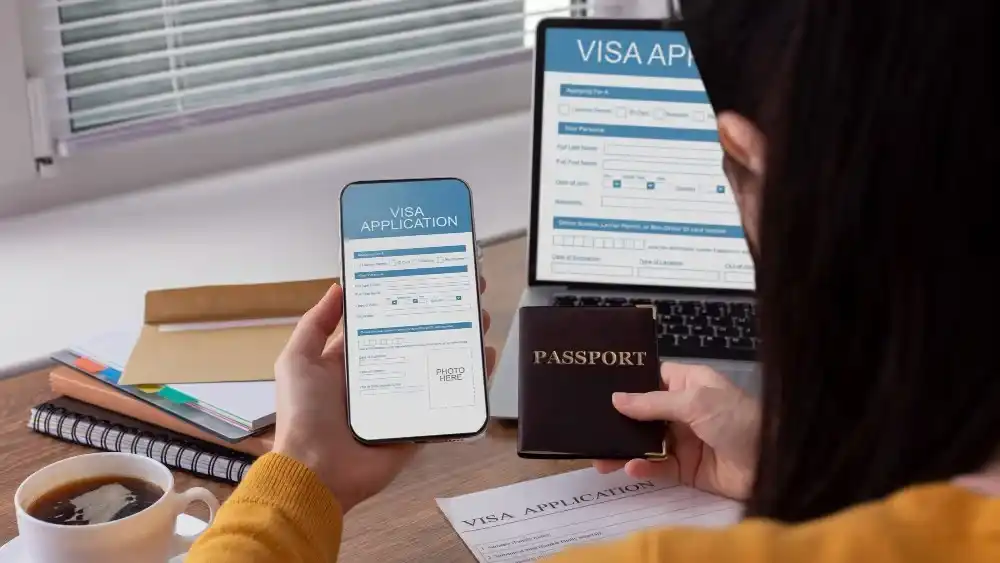 Person completing visa application on phone with passport and laptop. Beyond Border.