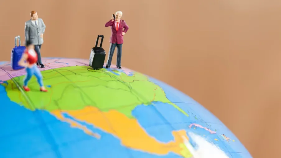 Mini figures with luggage on globe showing travel to the U.S. Beyond Border.