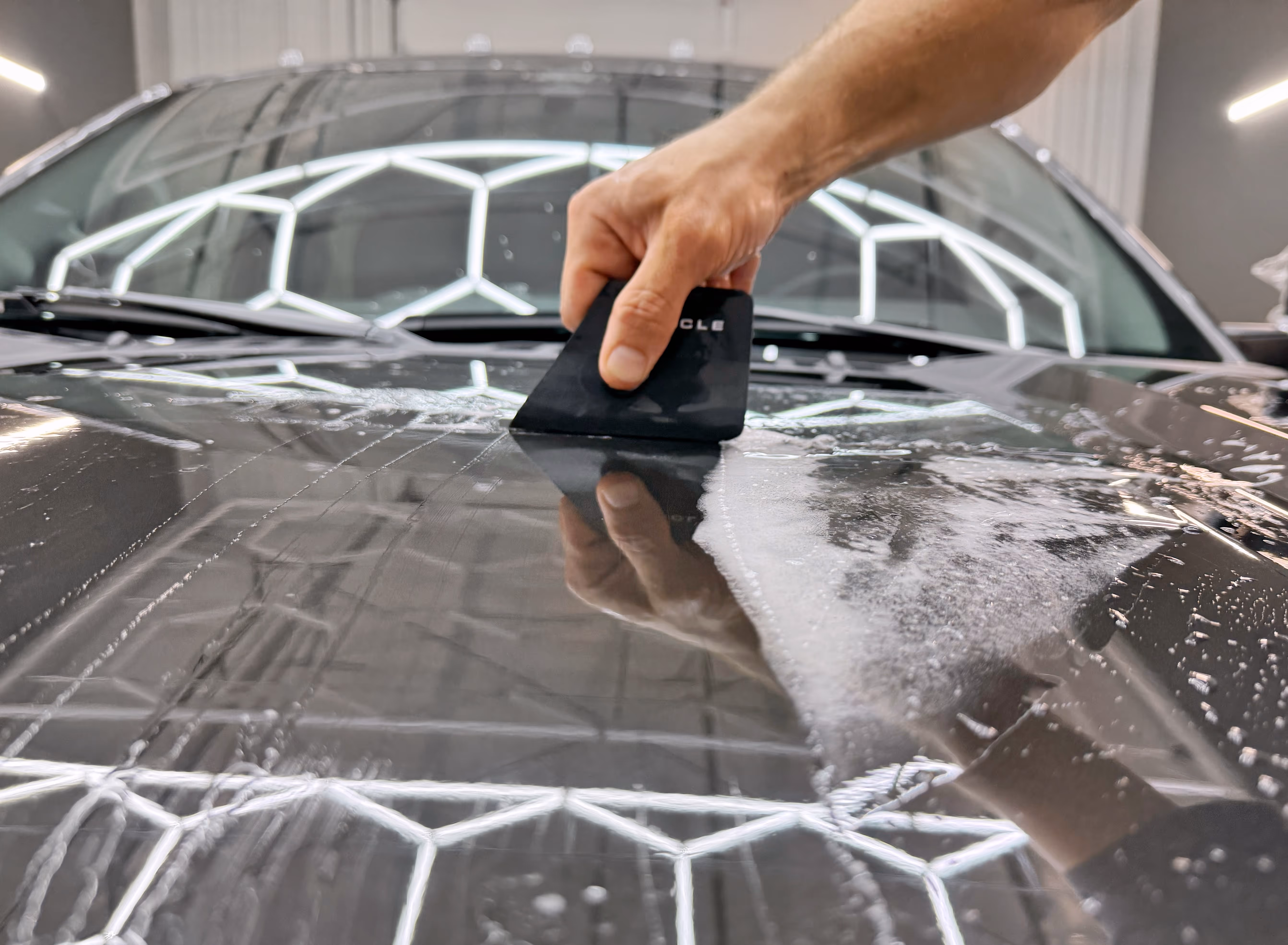 Scraping the excess liquid under the PPF film for a perfect paint protection film installation.