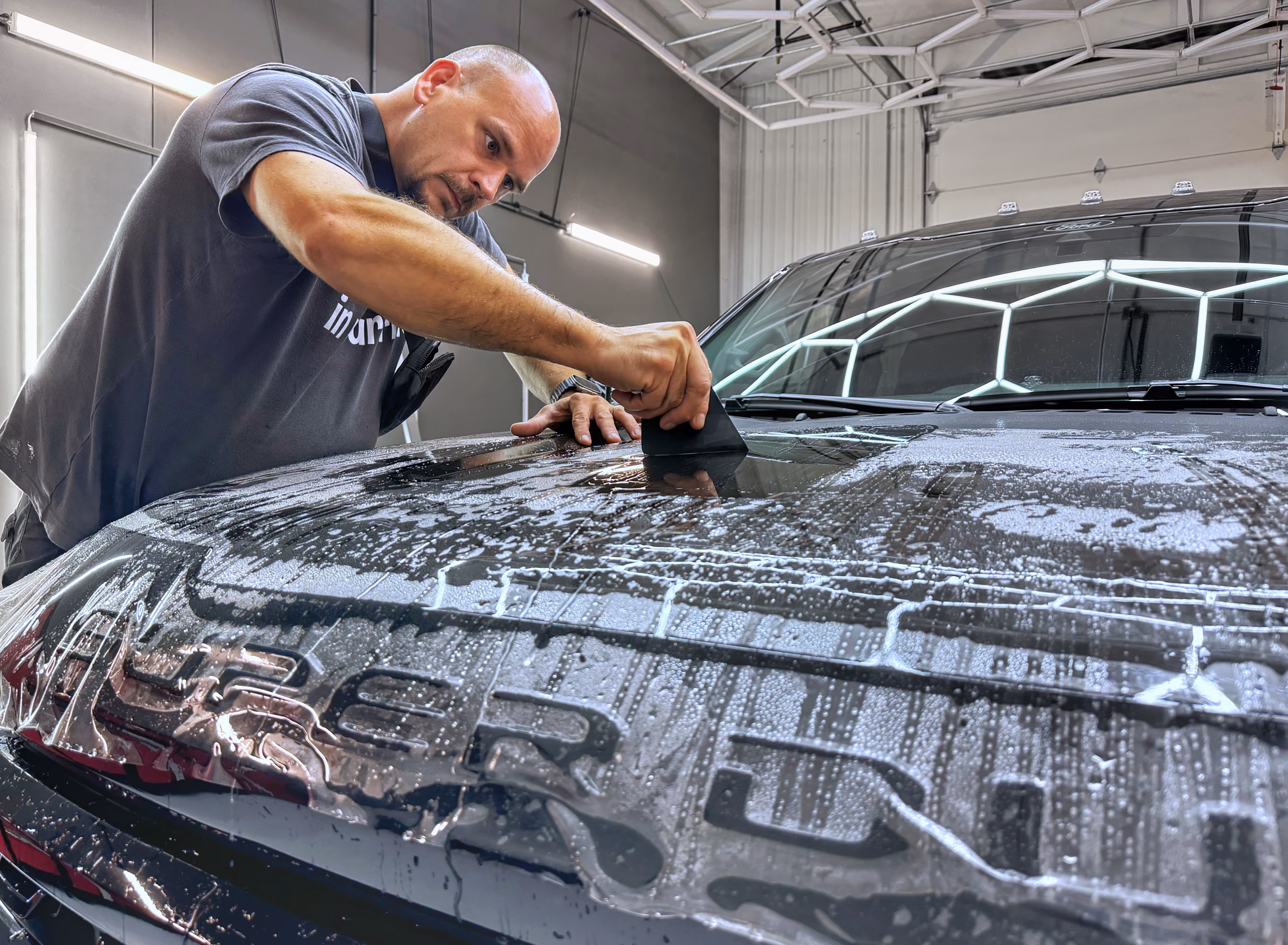 Wayne in the middle of a paint protection film (PPF) installation, scraping off the excess liquid underneath the film in Chattanooga shop.
