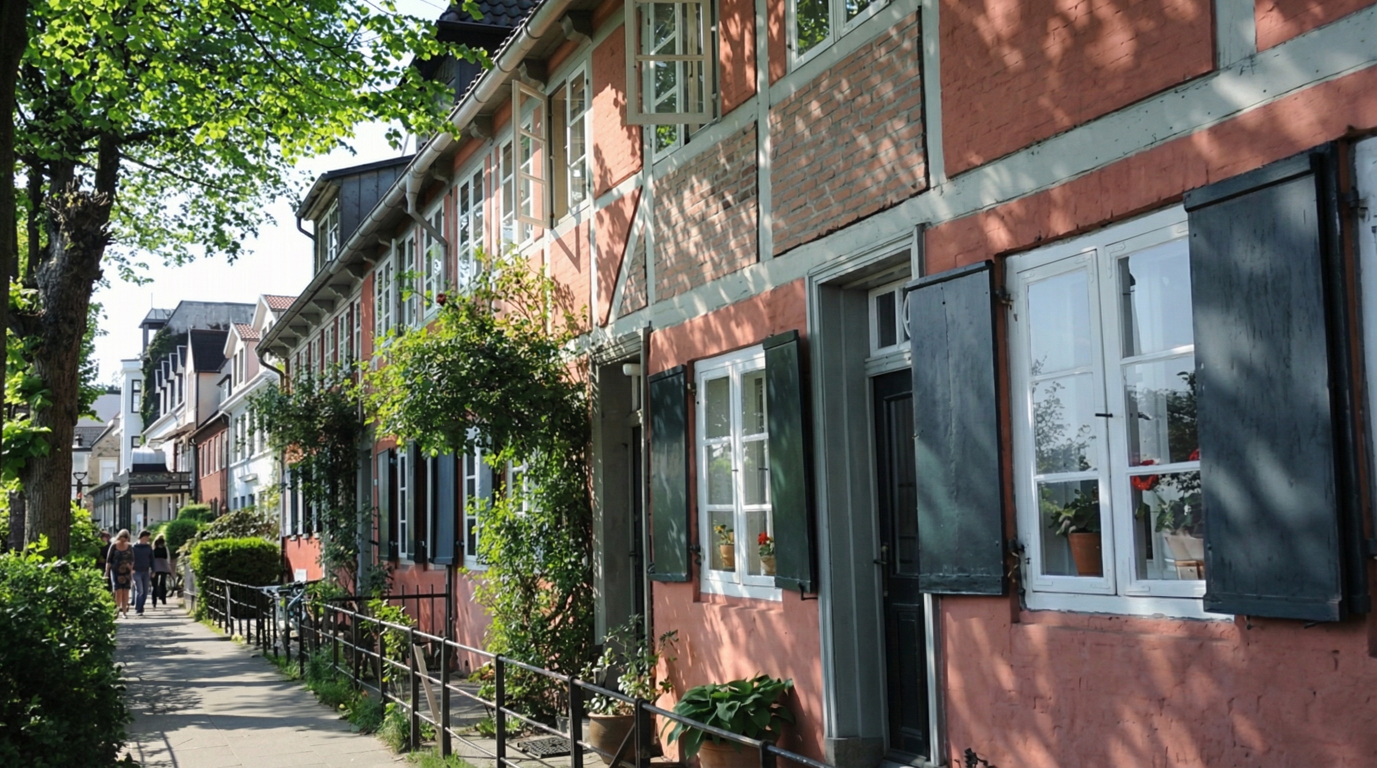 Reihe von Fachwerkhäusern mit roten Fassaden, weißen Fenstern und schwarzen Fensterläden an einem sonnigen Gehweg mit Bäumen in Othmarschen, Hamburg.
