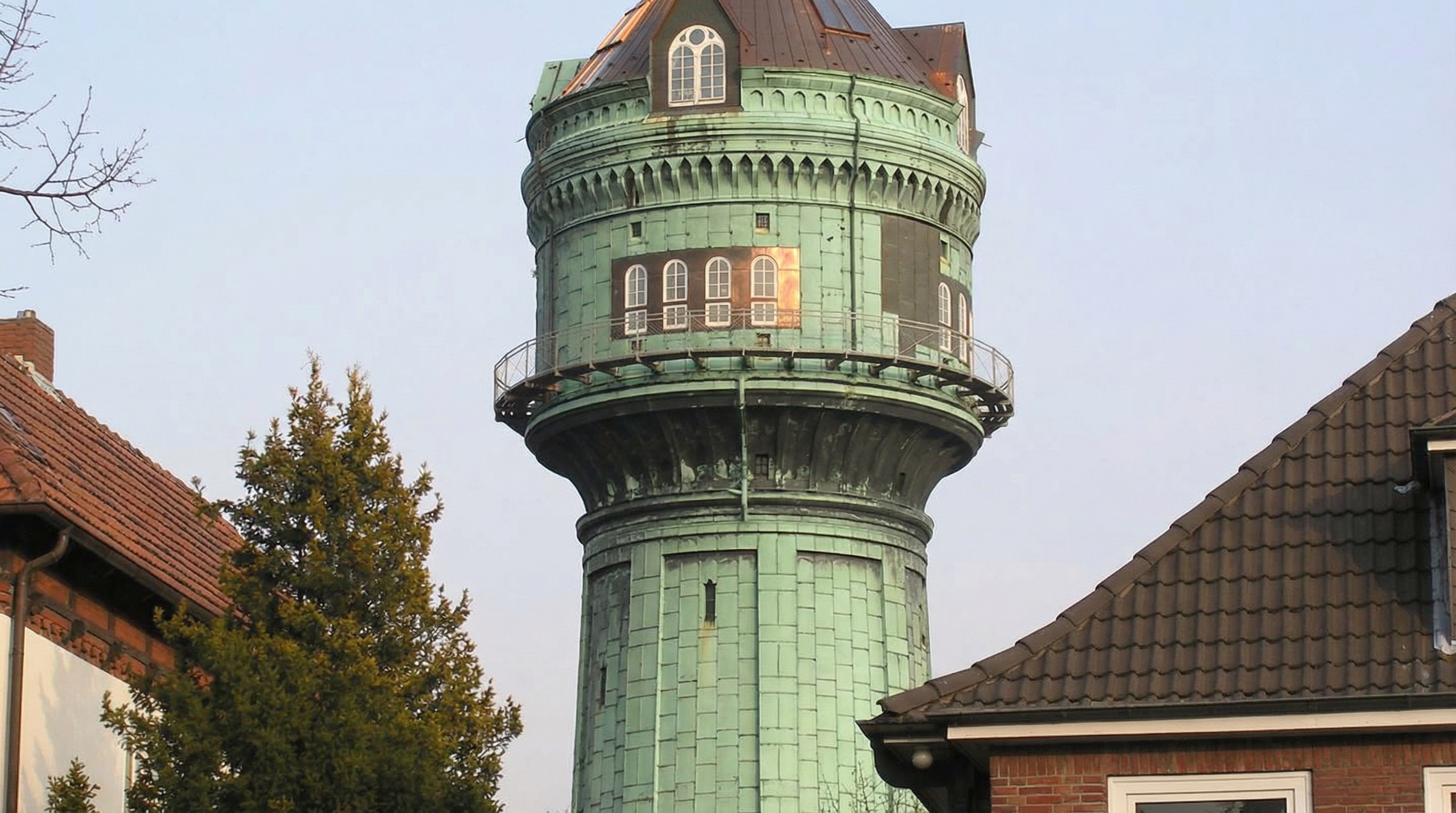 Grüner Wasserturm mit mehreren Fenstern und umlaufendem Geländer, umgeben von Bäumen und Dächern in Lokstedt, Hamburg.
