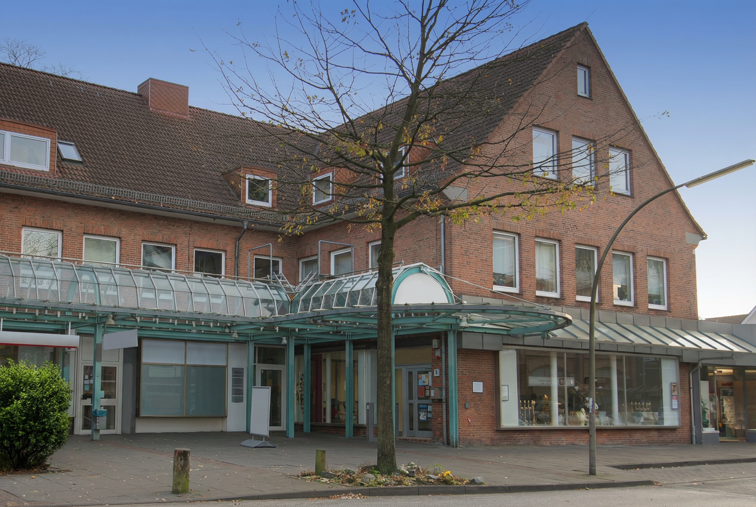 Zweistöckiges Backsteingebäude mit Satteldach, Glasvordach am Eingang und kahlem Baum davor in Eidelstedt, Hamburg.