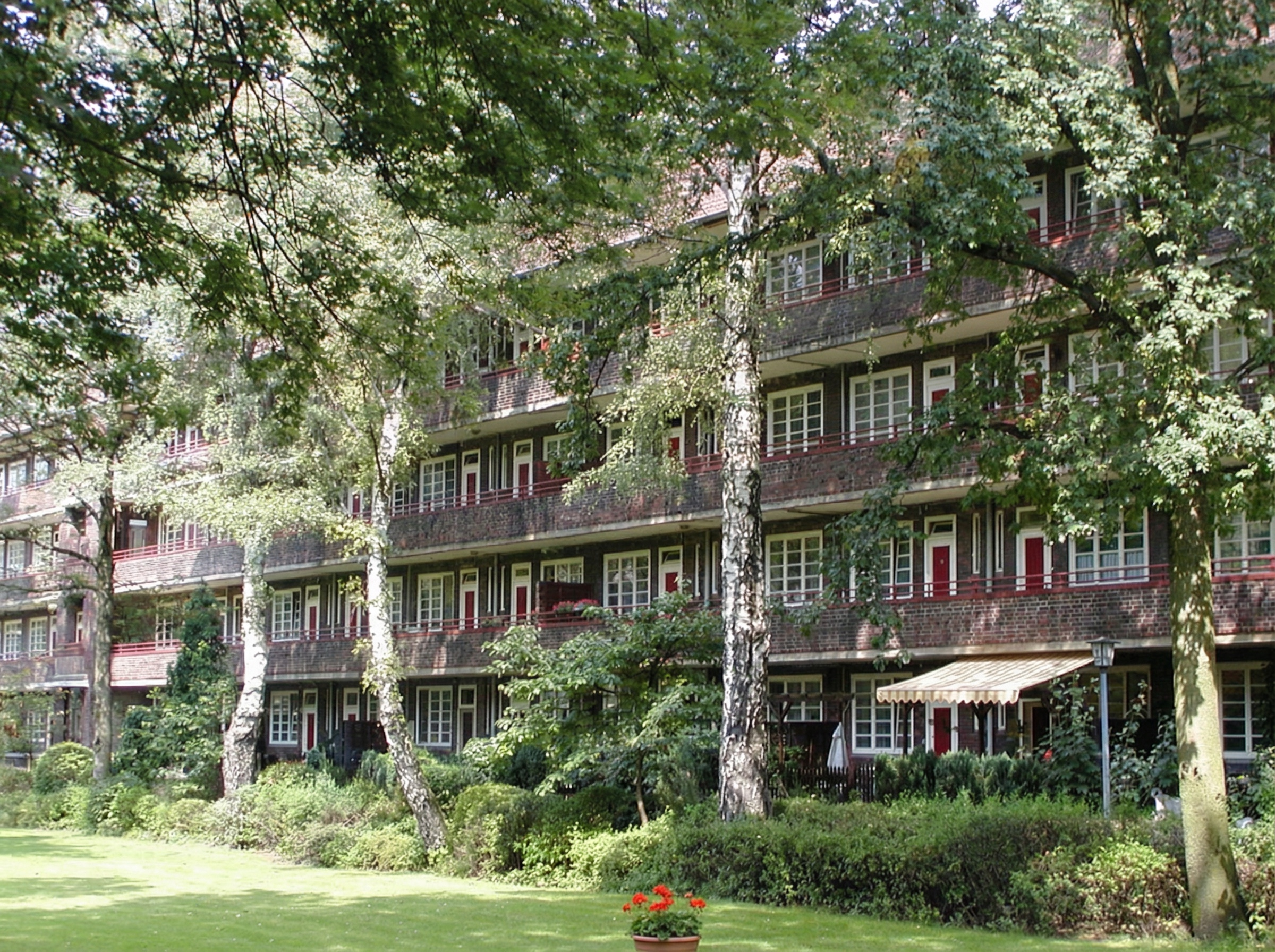 Mehrstöckiges Wohngebäude mit Balkonen, umgeben von Bäumen und Grünflächen im Stadtteil Dulsberg, Hamburg.