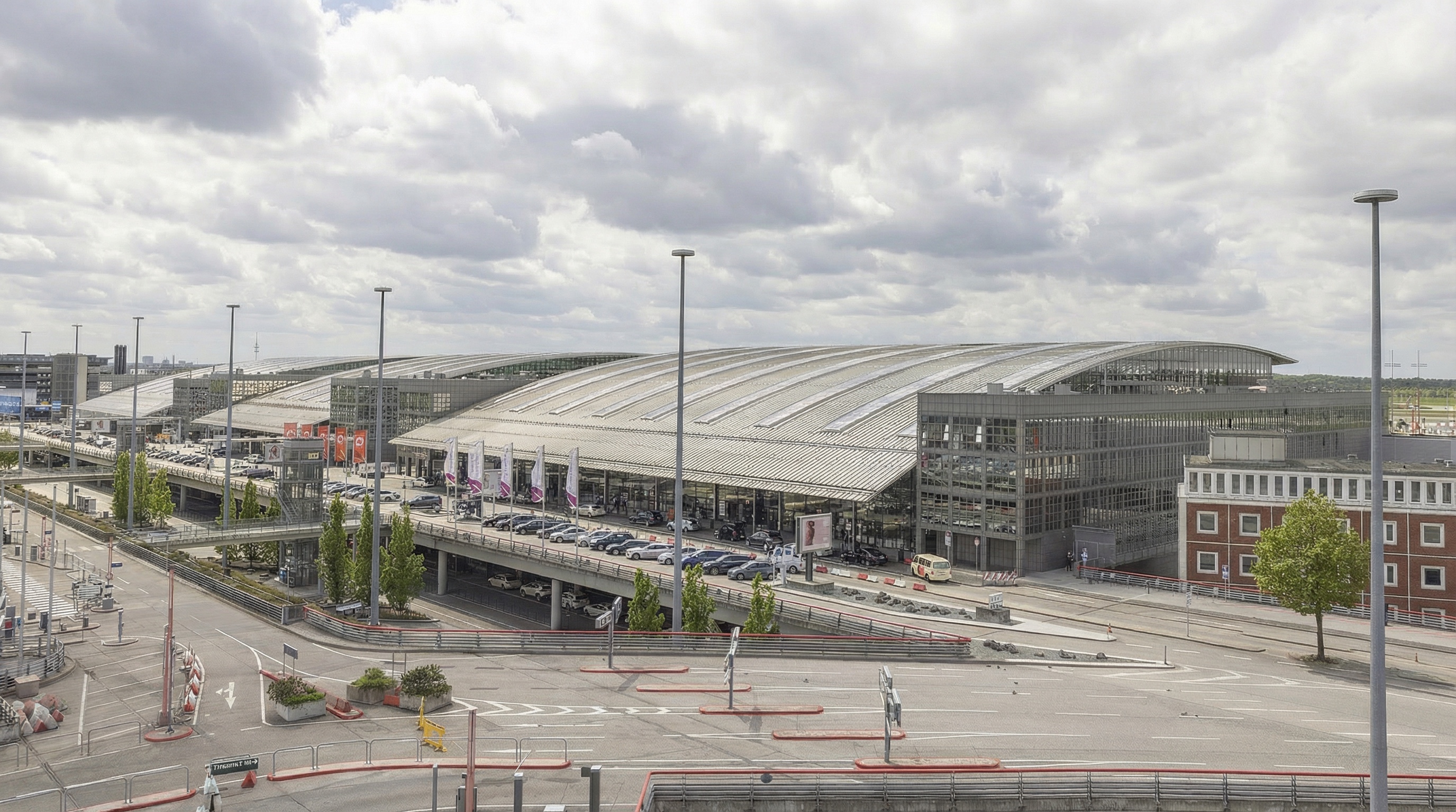 Großes, modernes Flughafengebäude mit gewölbtem Dach, davor Straßenkreuzung und mehrere Bäume in Fuhlsüttel, Hamburg.