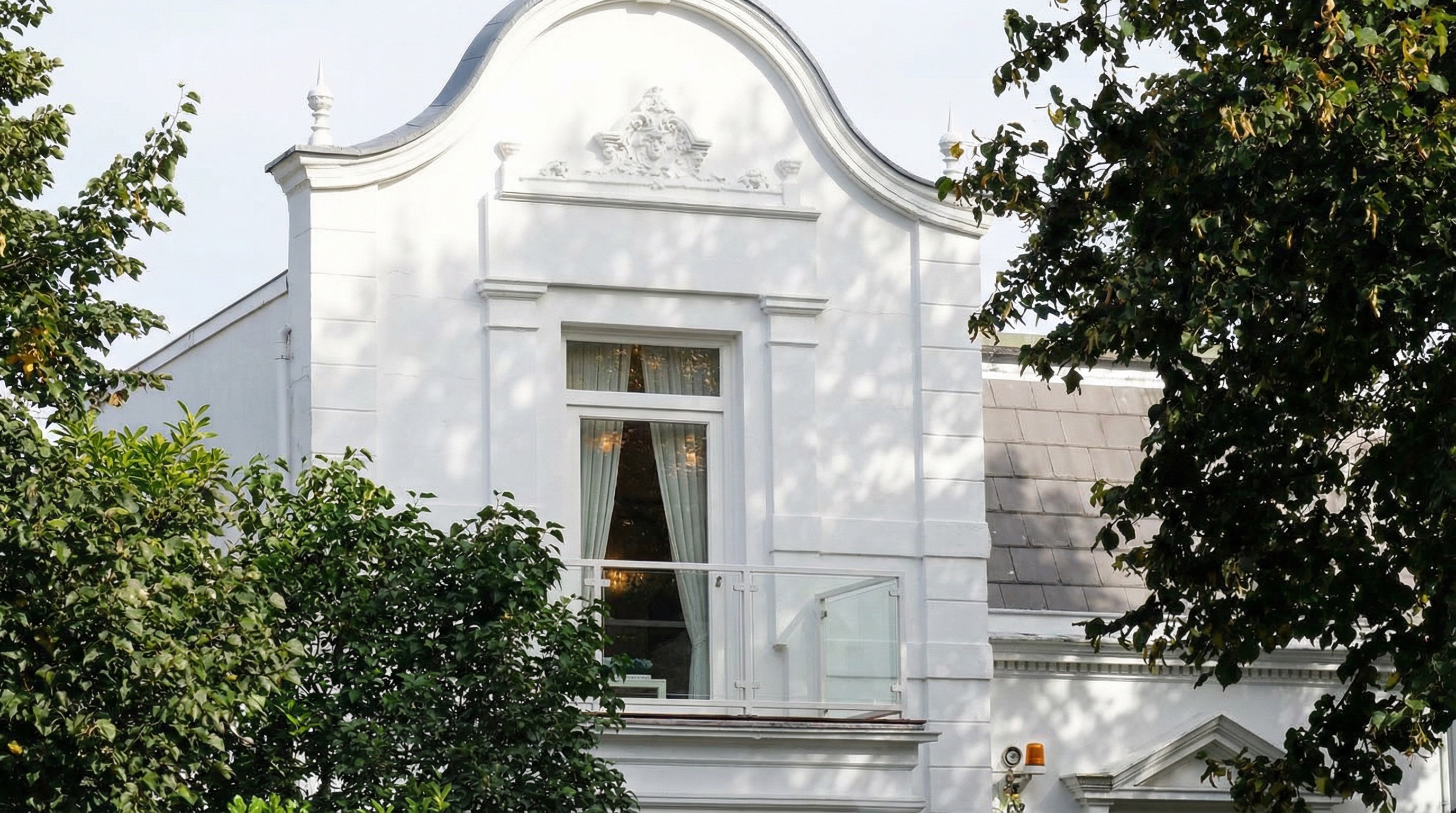 Fassade eines Gründerzeithauses mit geschwungenem Giebel, Fenster mit Gardinen und umliegenden Bäumen in Marienthal, Hamburg.
