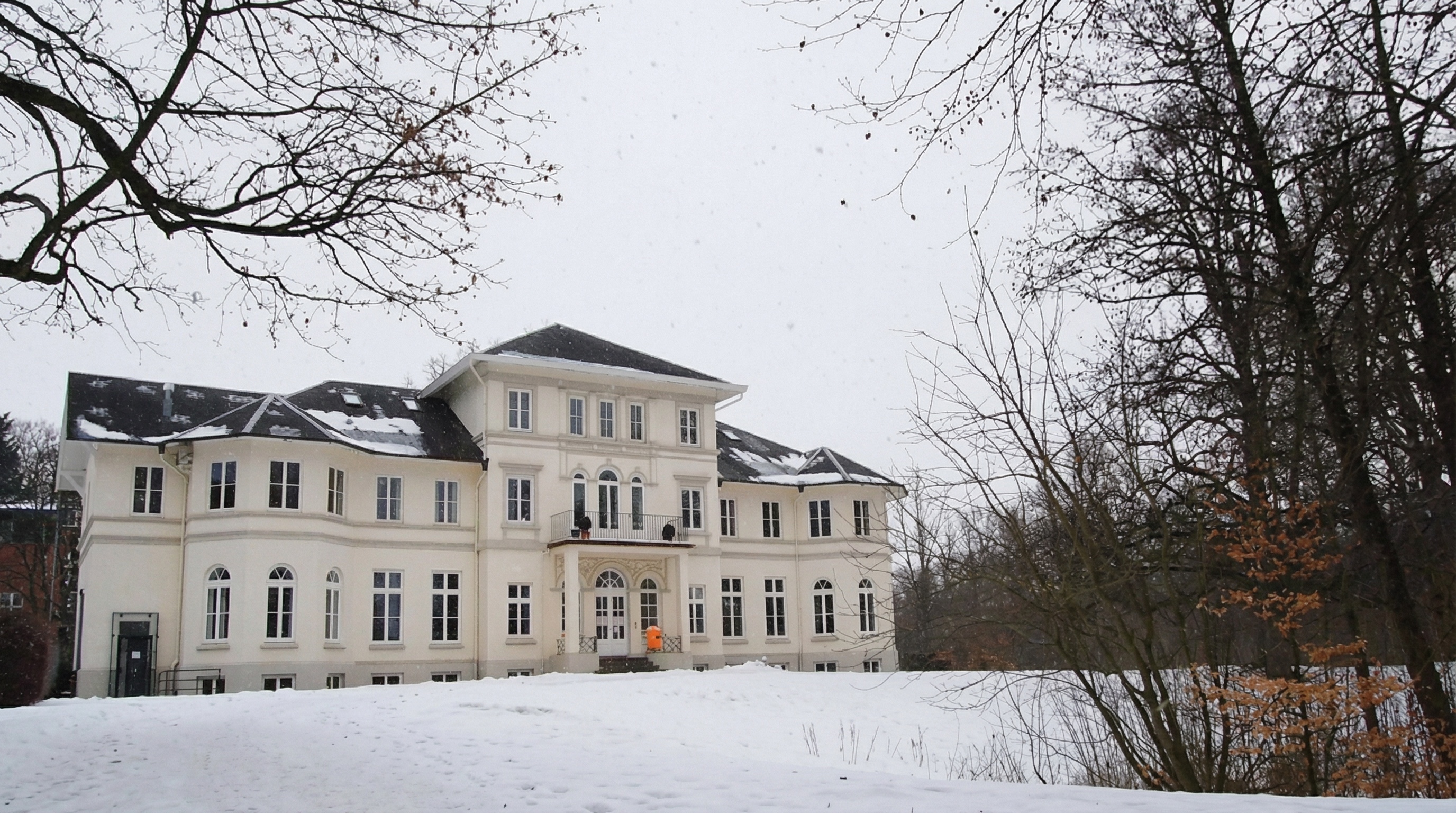 Großes, weißes Herrenhaus mit mehreren Fenstern und verschneitem Garten im Vordergrund, kahle Bäume rechts und links in Farmsen Berne, Hamburg.
