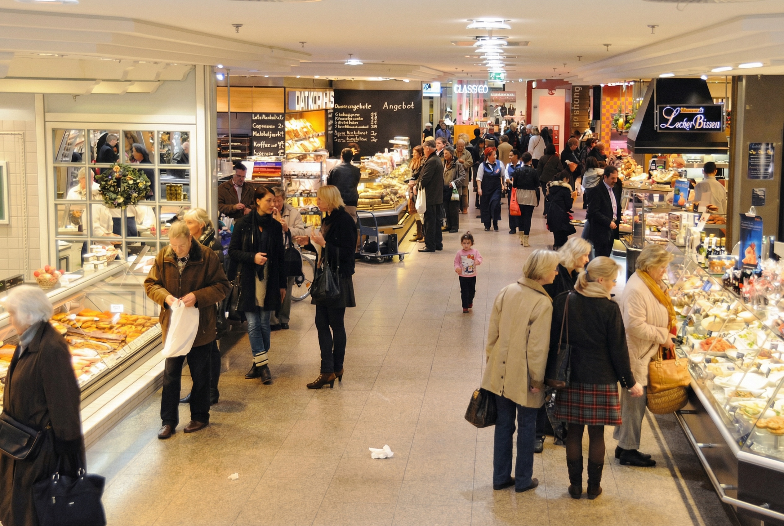 Innenansicht eines belebten Einkaufszentrums mit mehreren Verkaufsständen und Menschen, die einkaufen und sich unterhalten in Poppenbüttel, Hamburg.