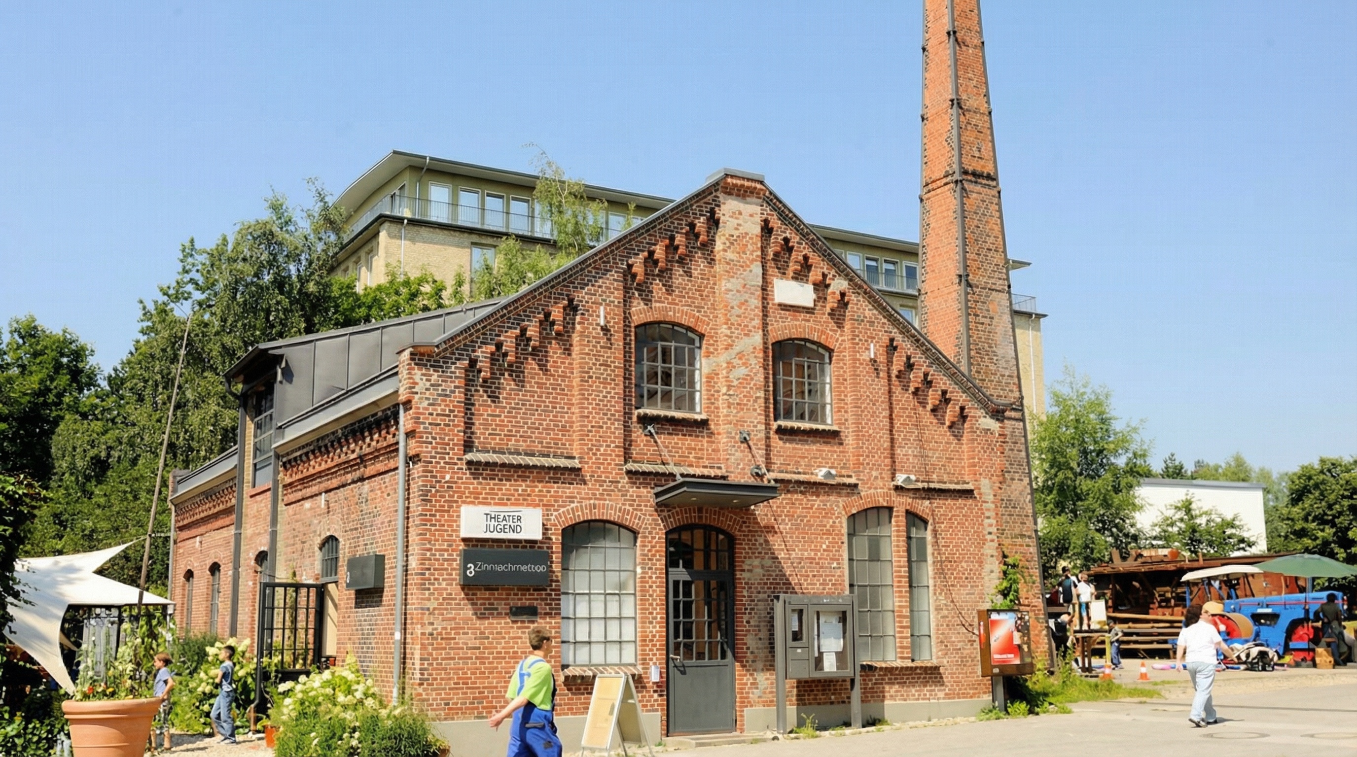 Rustikales Backsteingebäude in industriellem Stil mit Schornstein, mehreren Fenstern und einem Schild mit der Aufschrift 'THEATER MAGAZIN' in der Alten Zinnschmelze, Barmbek-Nord, Hamburg.