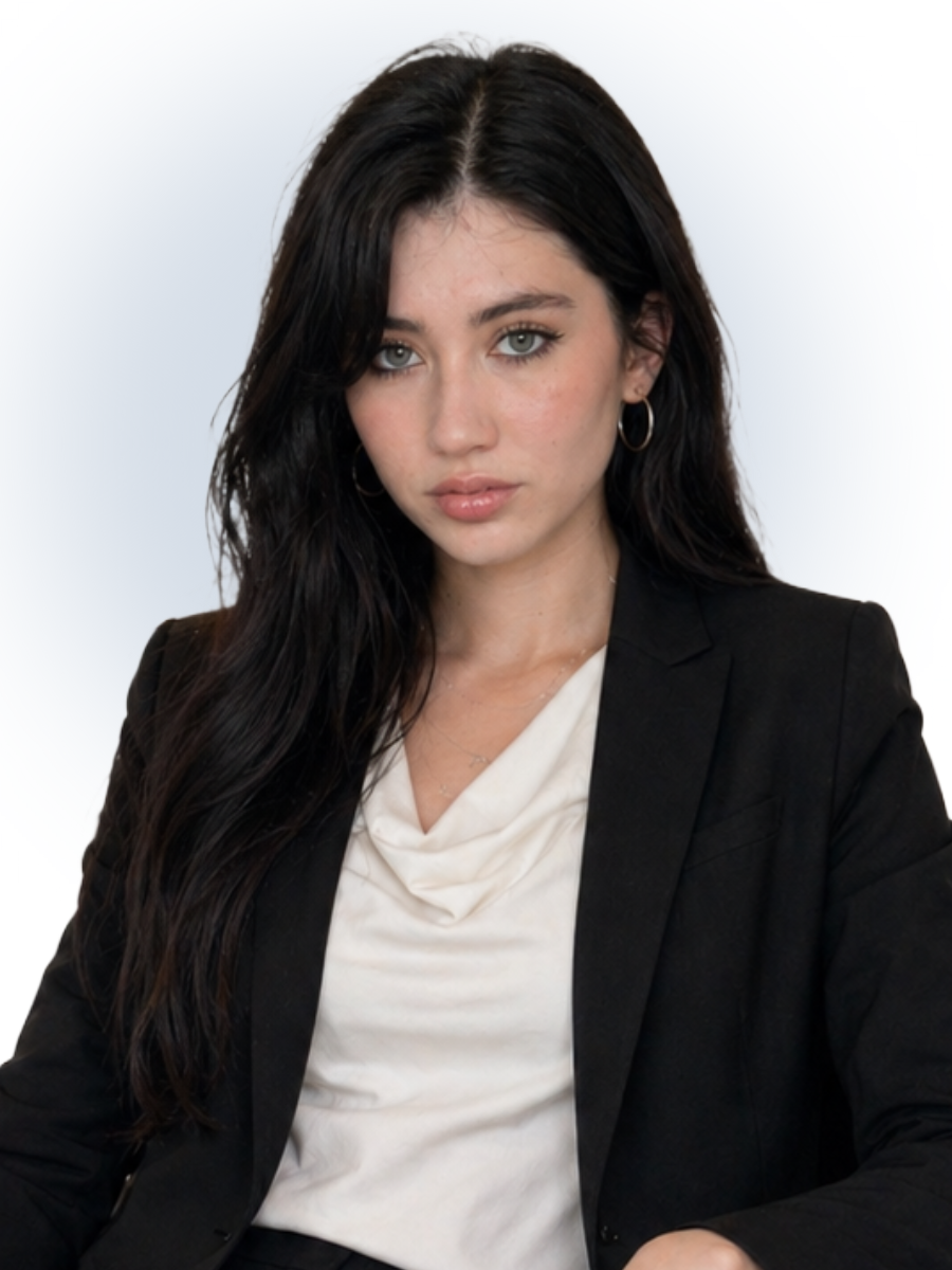 Young woman with long dark hair wearing a black blazer and white blouse against a light background.