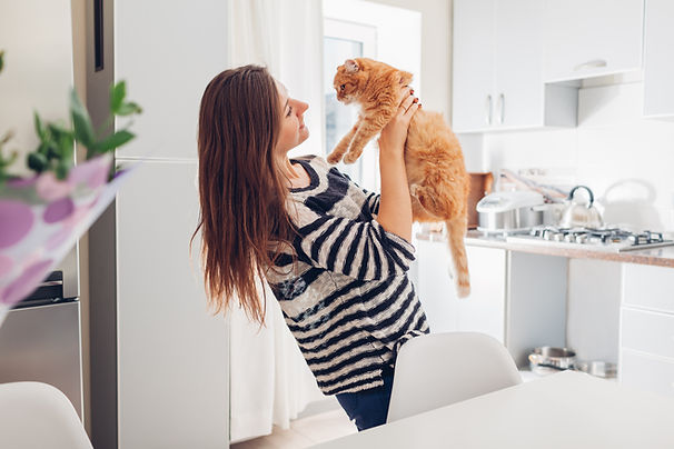 A woman holding an orange cat in her arms, smiling at it, in a modern kitchen setting.