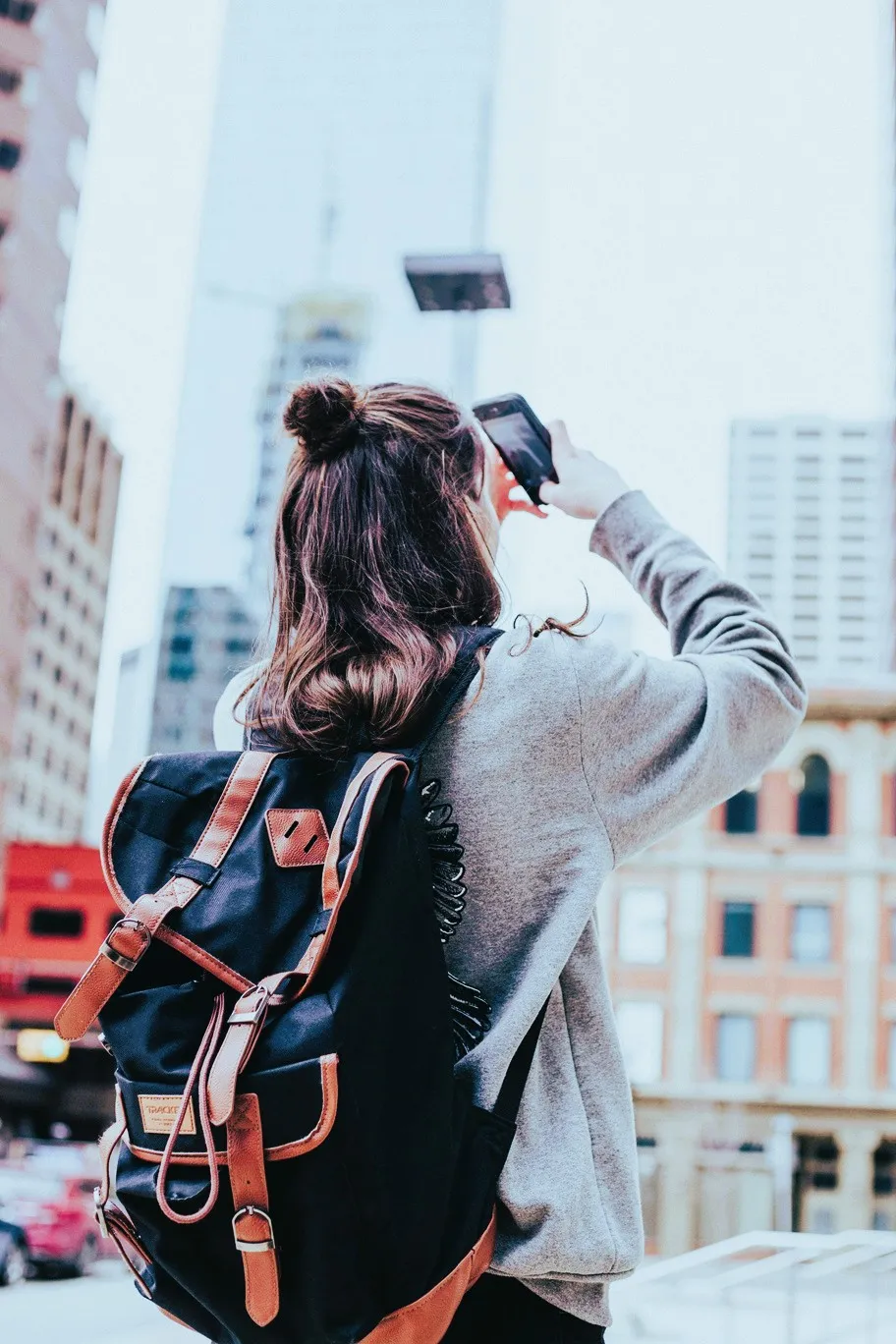 A girl taking a photo of a tall building in the city.