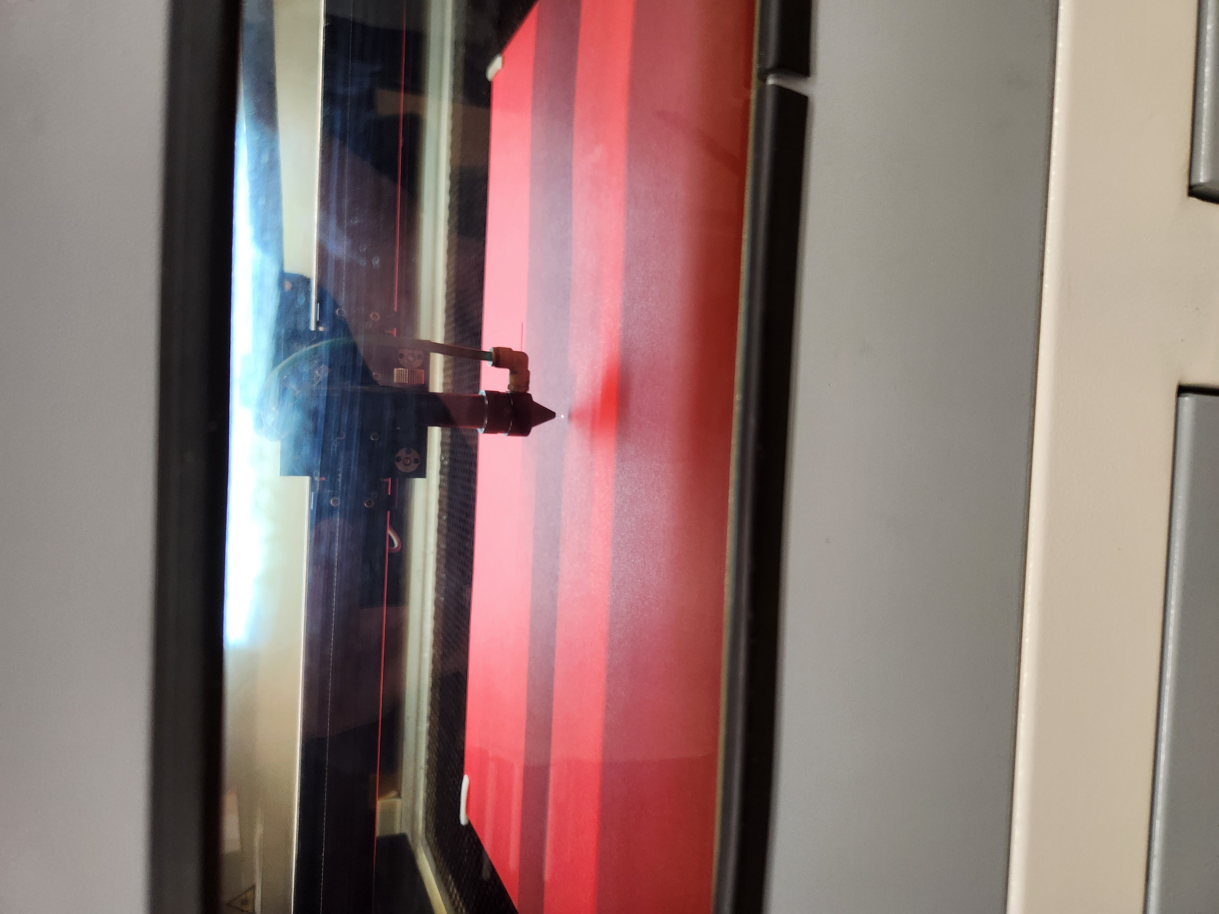 Laser cutting machine operating on a red sheet inside an enclosed workspace.
