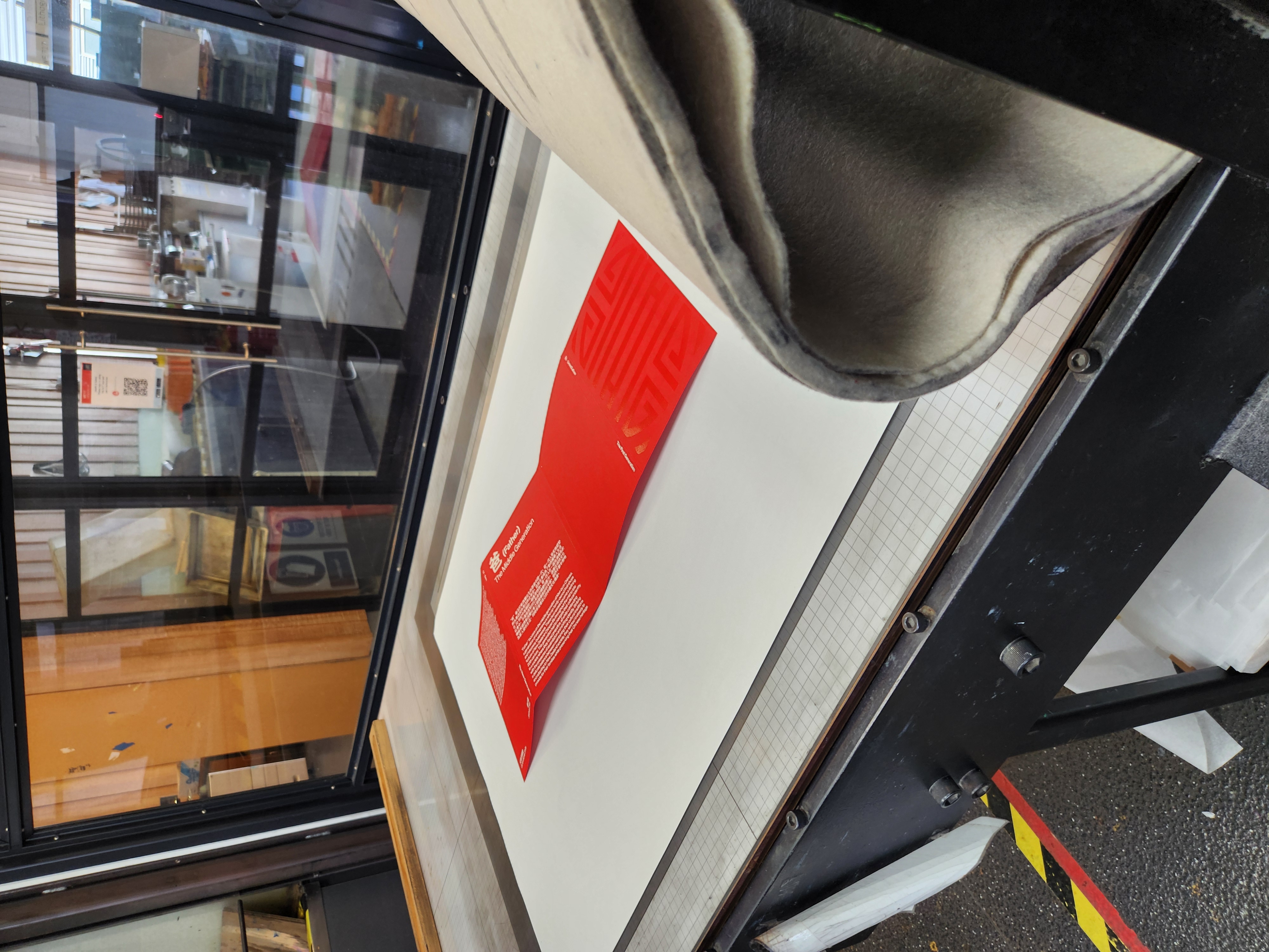 Red folded printed sheet on a large flat printing press bed in a workshop.