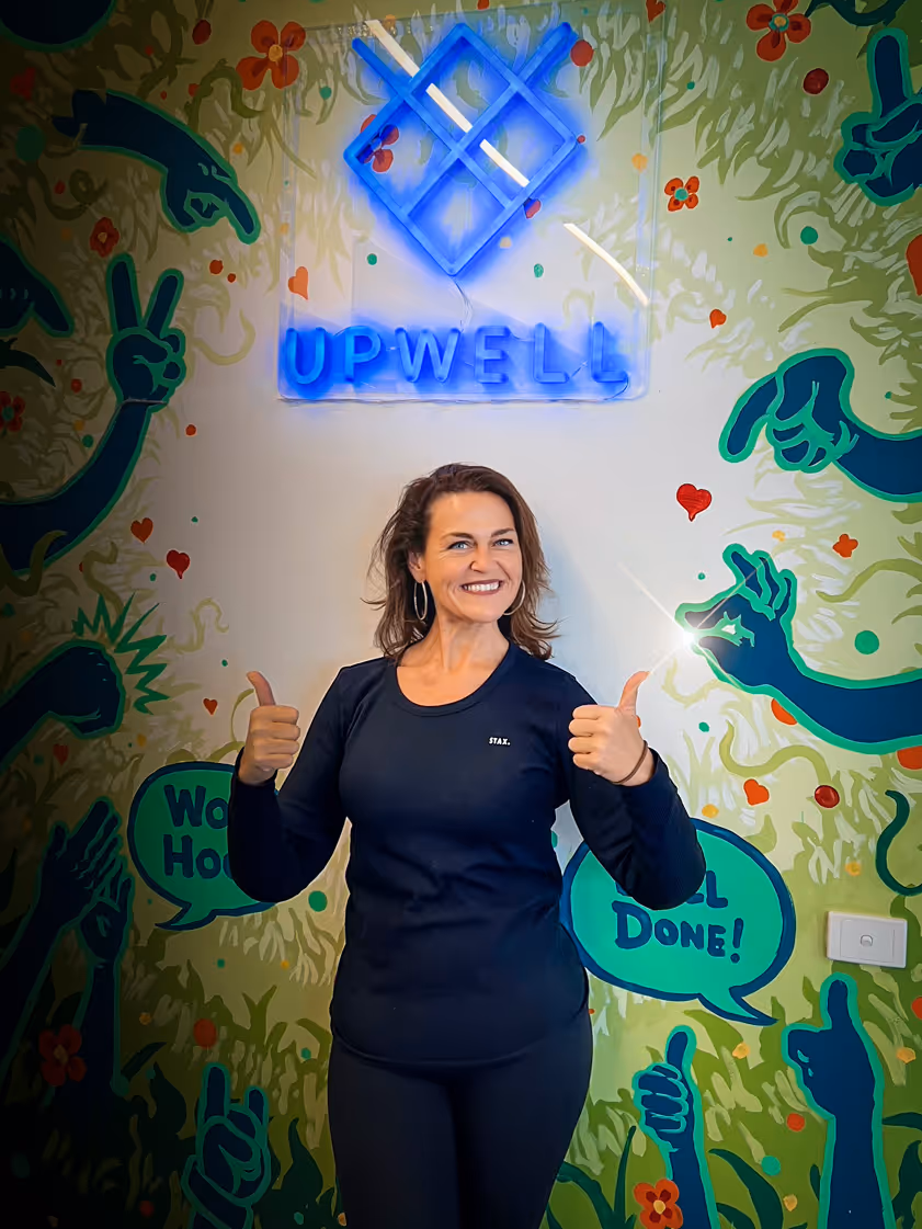 Smiling woman in black clothing giving thumbs up in front of a colorful wall with blue neon UPWELL sign and congratulatory text bubbles.