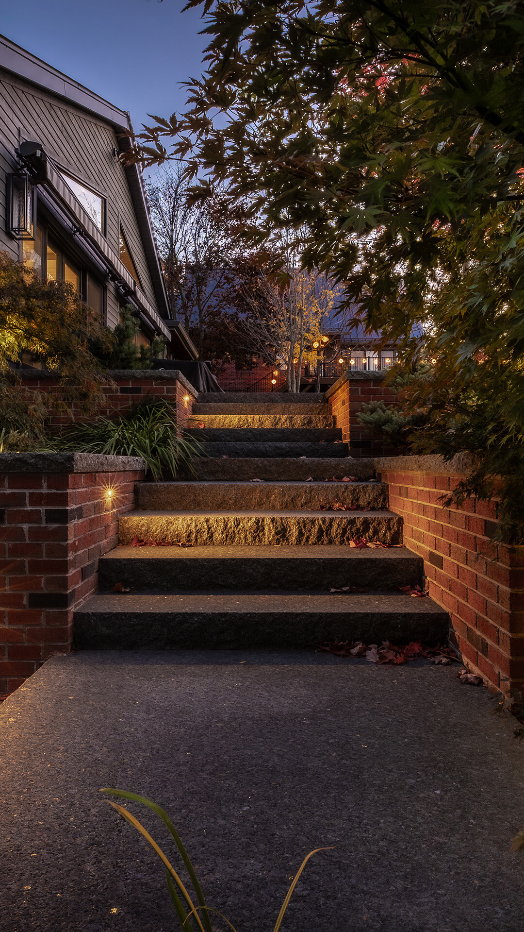 Stone steps lined with brick walls and illuminated with small lights leading to a house in the evening.