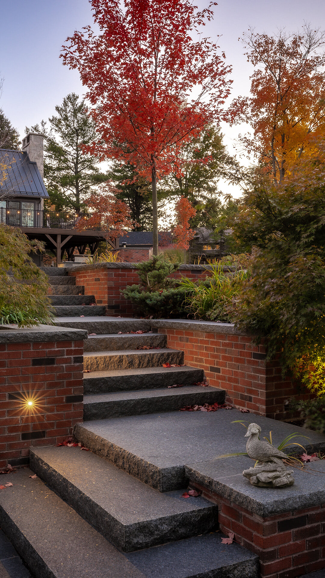 Outdoor stone staircase with red brick walls, autumn foliage, and a stone duck statue on the right corner.