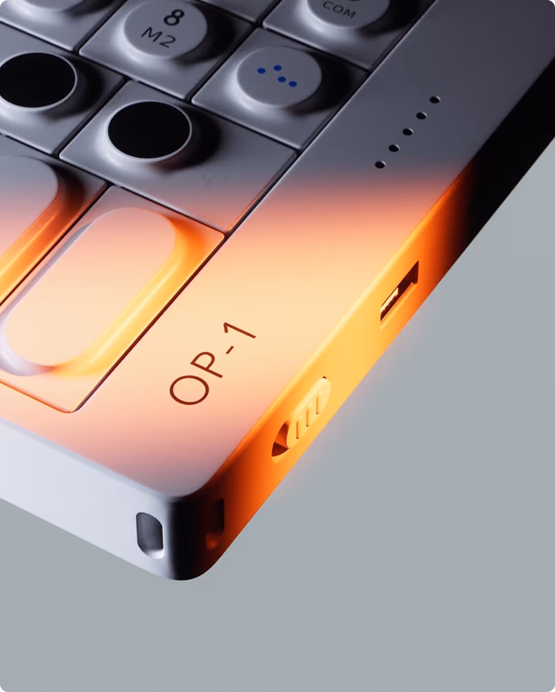 Close-up of the OP-1 synthesizer showing buttons, a USB port, and an orange-lit side switch.