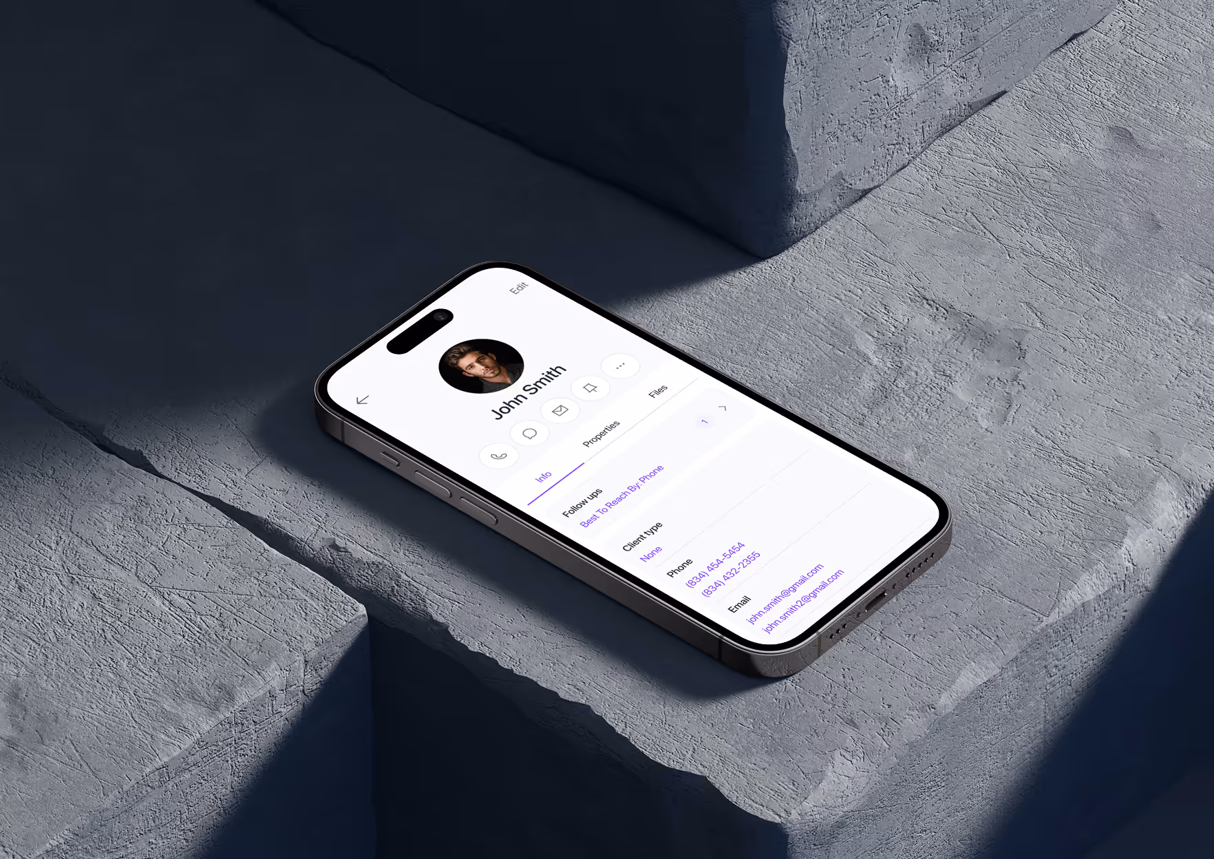 Smartphone showing a contact profile for John Smith with phone numbers and emails on a gray stone surface.
