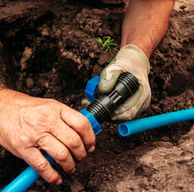 Hands assembling irrigation pipes during professional sprinkler system installation for gardens and lawns