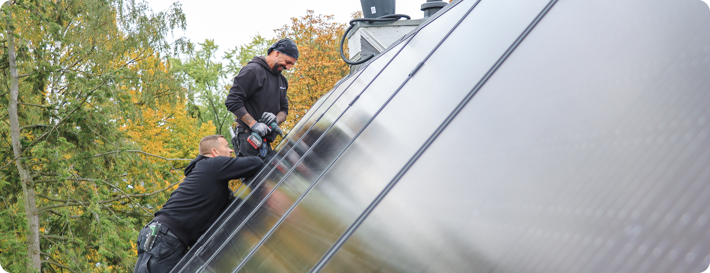 Zwei Installateure sind zu sehen, wie sie auf dem Dach eine Solaranlage befestigen.