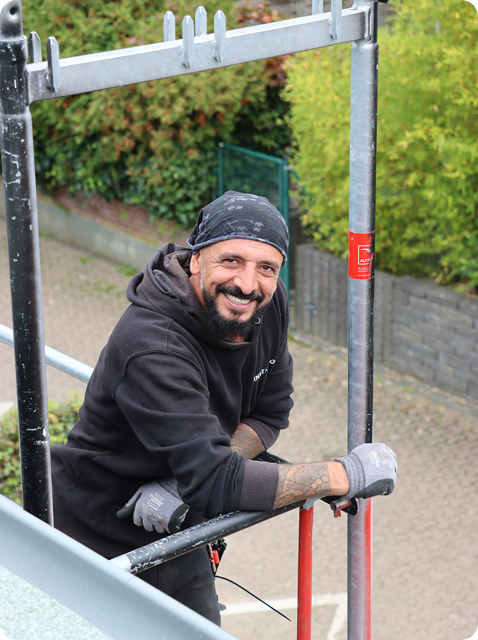 Ein Installateur steht auf einem Baugerüst und lächelt in die Kamera