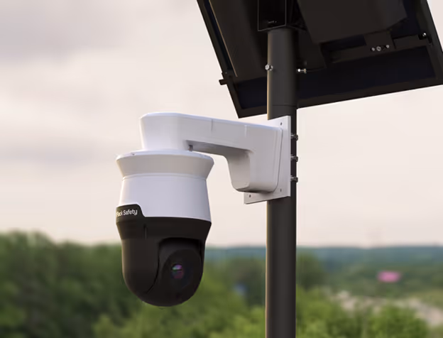 Security camera mounted on a pole with a solar panel, overlooking an outdoor area with trees.
