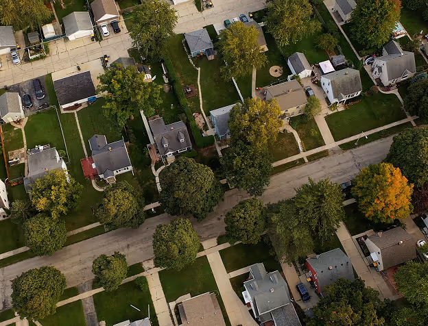 Aerial view of a suburban neighborhood with houses, trees, sidewalks, and cars parked along the streets.