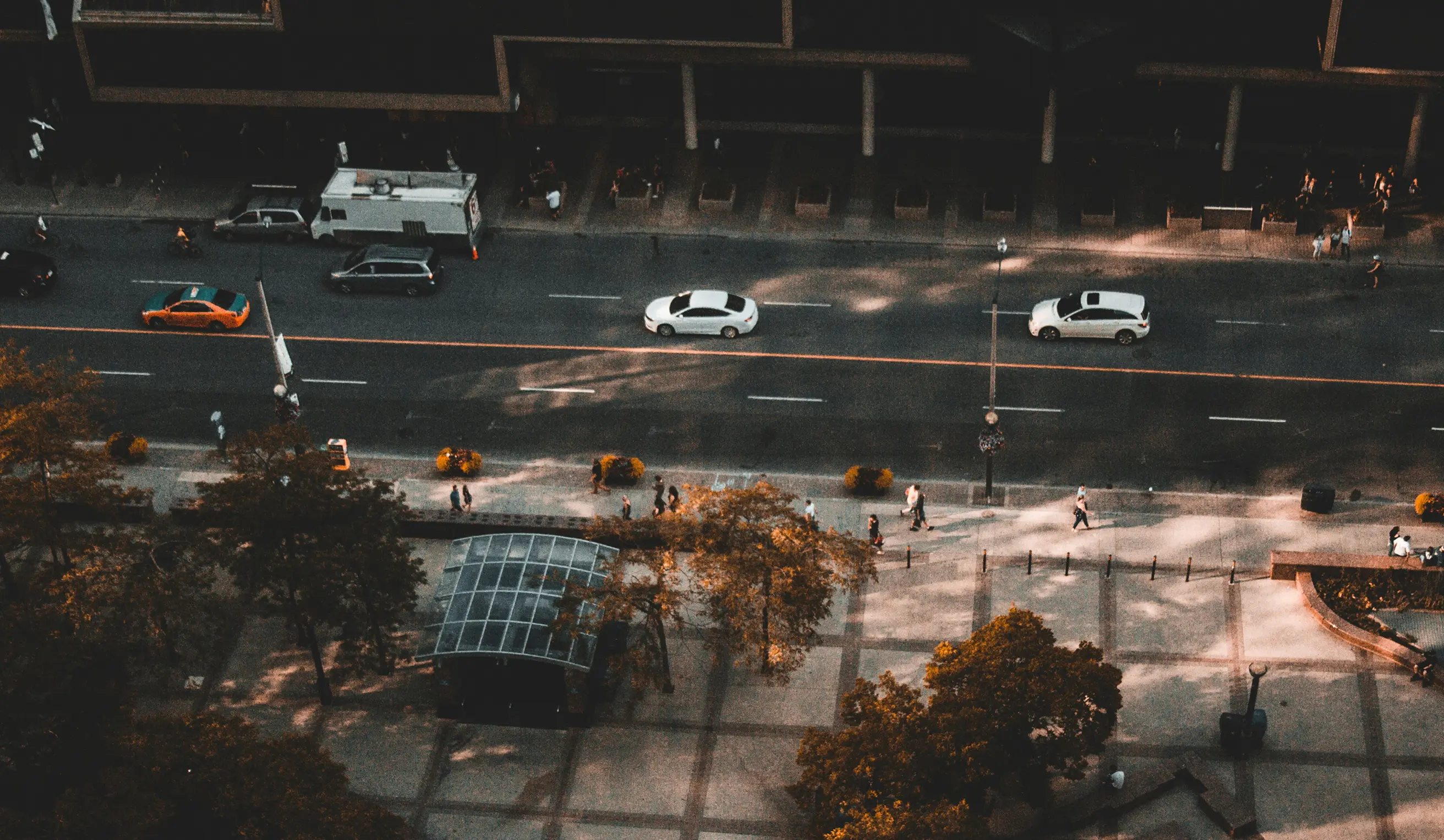 Aerial view of a street with cars, trees, and people walking on the sidewalk and plaza.
