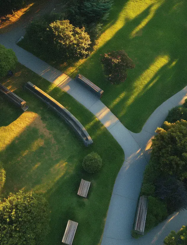 Aerial view of park pathways with benches, green grass, and trees casting long shadows in sunlight.