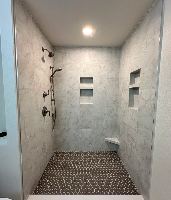 Modern bathroom after tub to shower conversion featuring a walk-in shower with marble-style wall tiles, built-in niches, bronze fixtures, and hexagon floor tiles