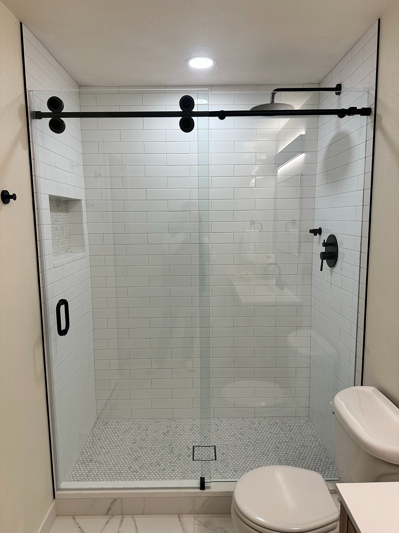 Contemporary bathroom with walk-in shower, sliding glass doors, white subway tile walls, matte black fixtures, and hexagon tile shower floor
