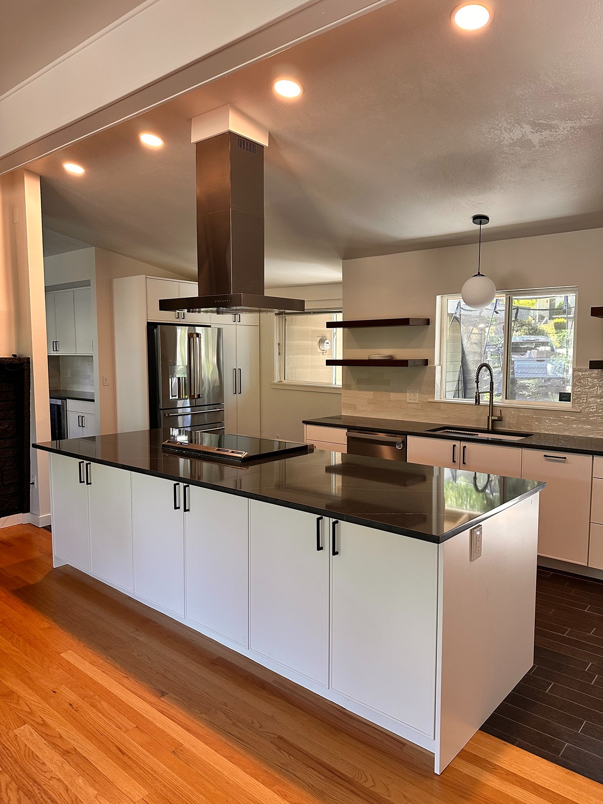 Modern white kitchen with large island, dark quartz top, and stainless range hood