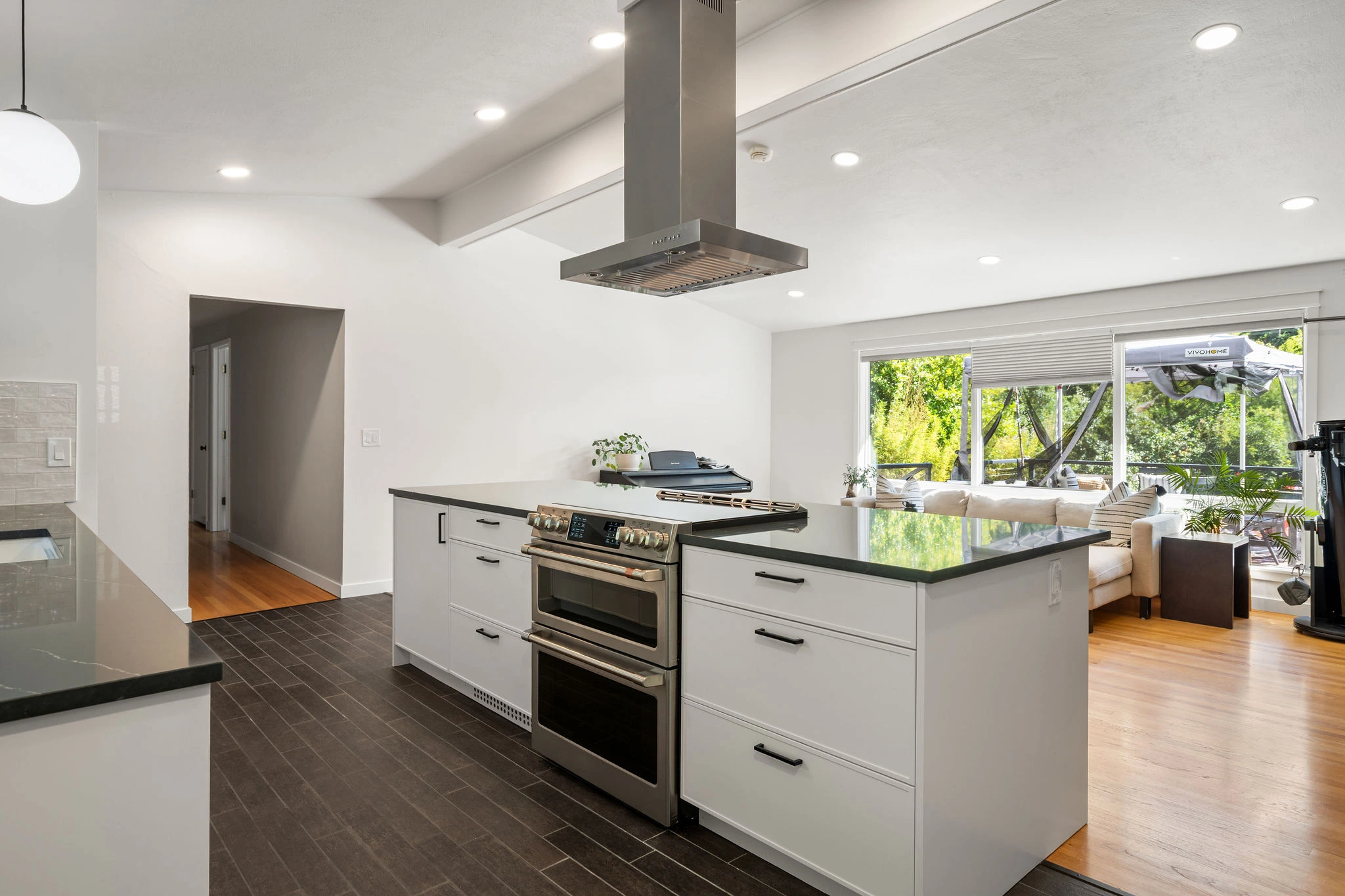 Open-concept kitchen renovation featuring a central island with double oven, dark tile flooring, and custom white cabinetry.
