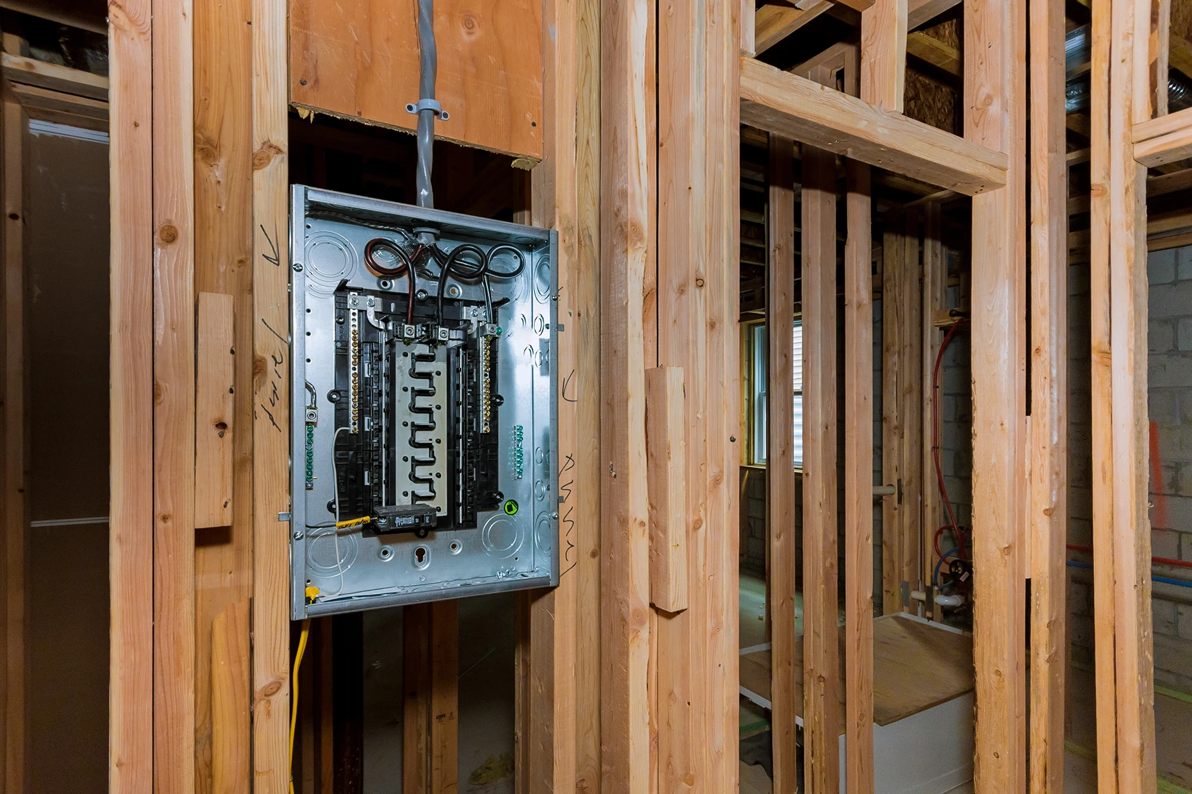Rough-in electrical panel installation inside exposed wood stud wall framing during home renovation.