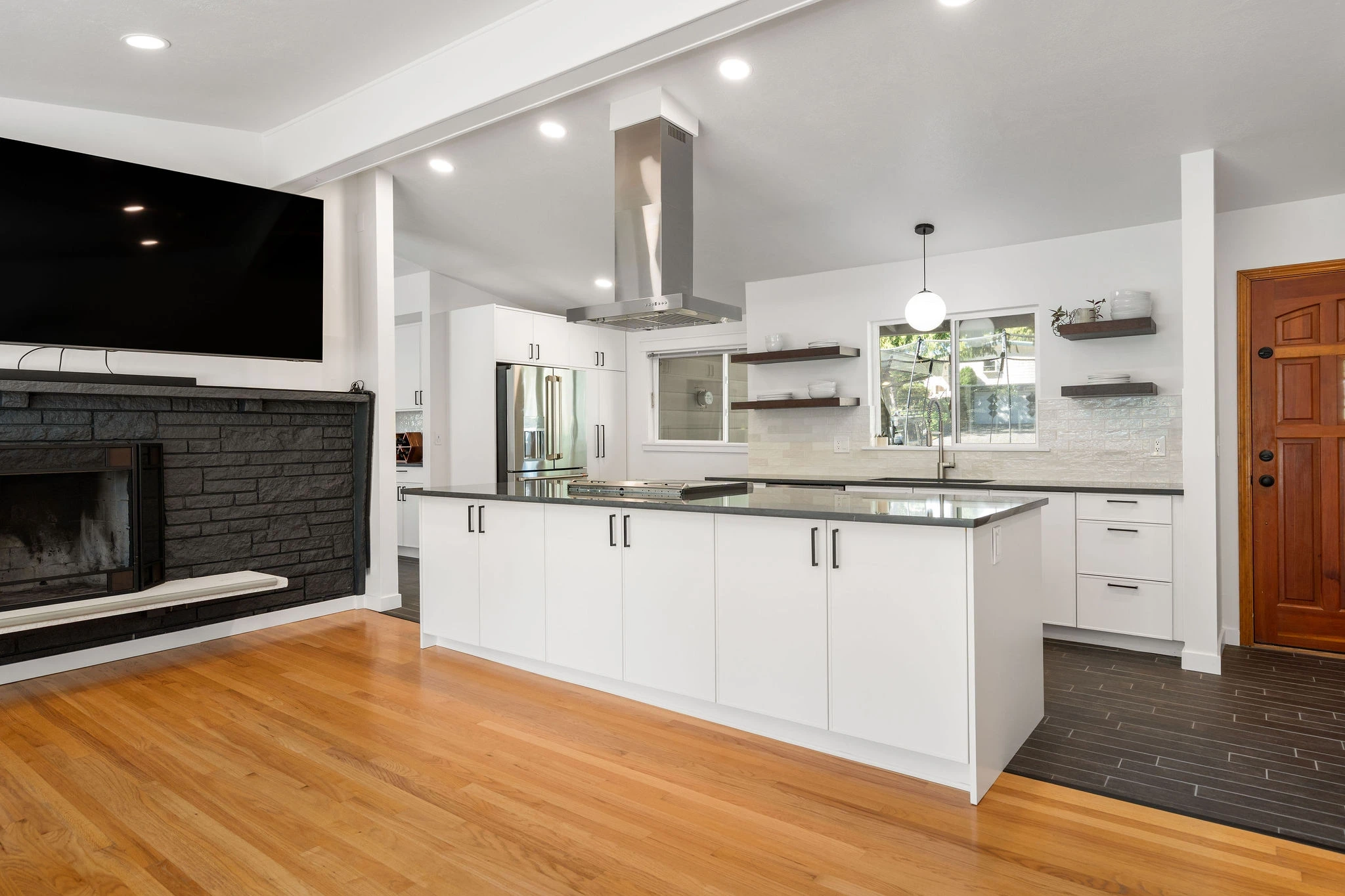 Remodeled kitchen with a white island, dark stone fireplace, and hardwood floors