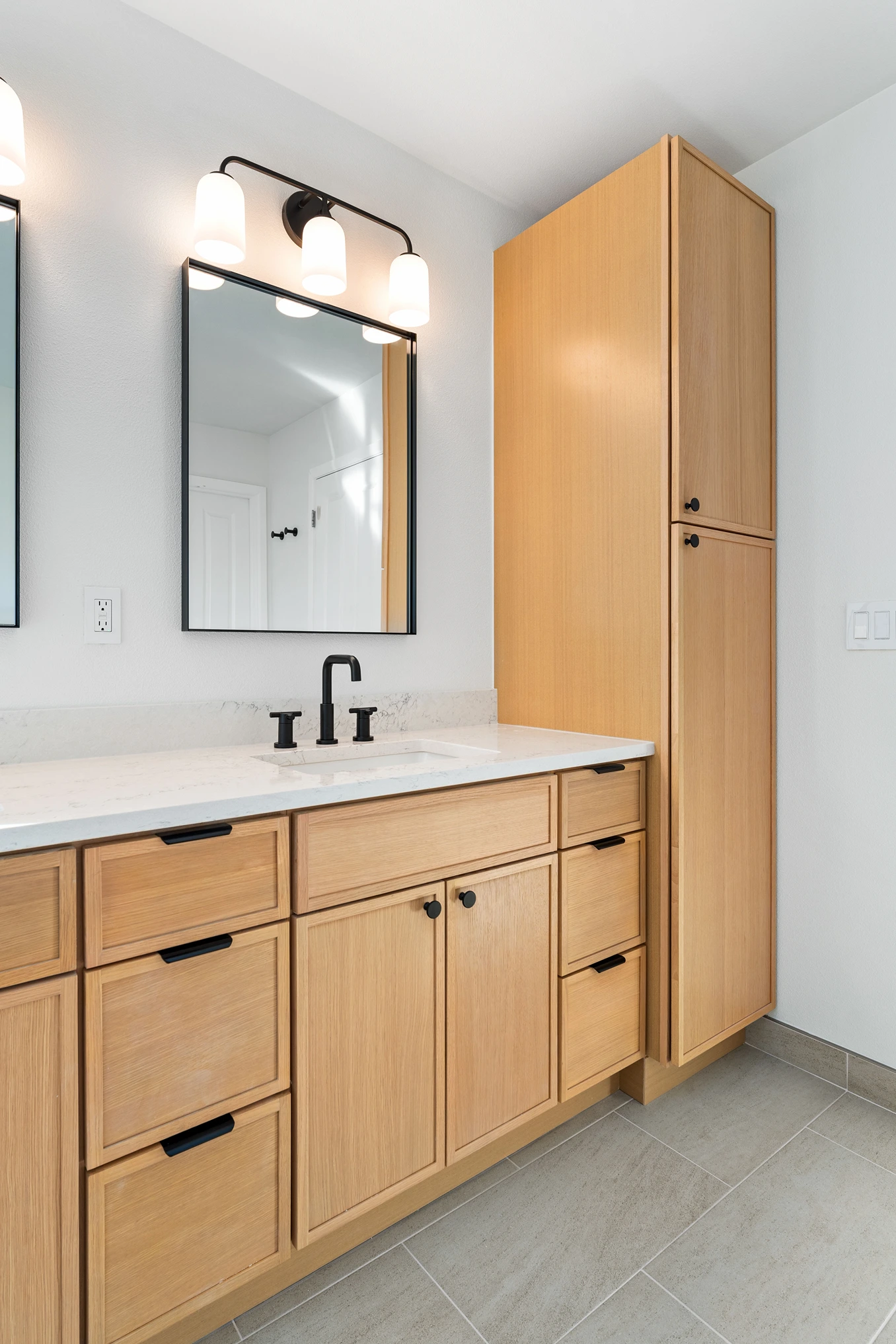 Natural wood bathroom vanity with tall storage cabinet and black fixtures