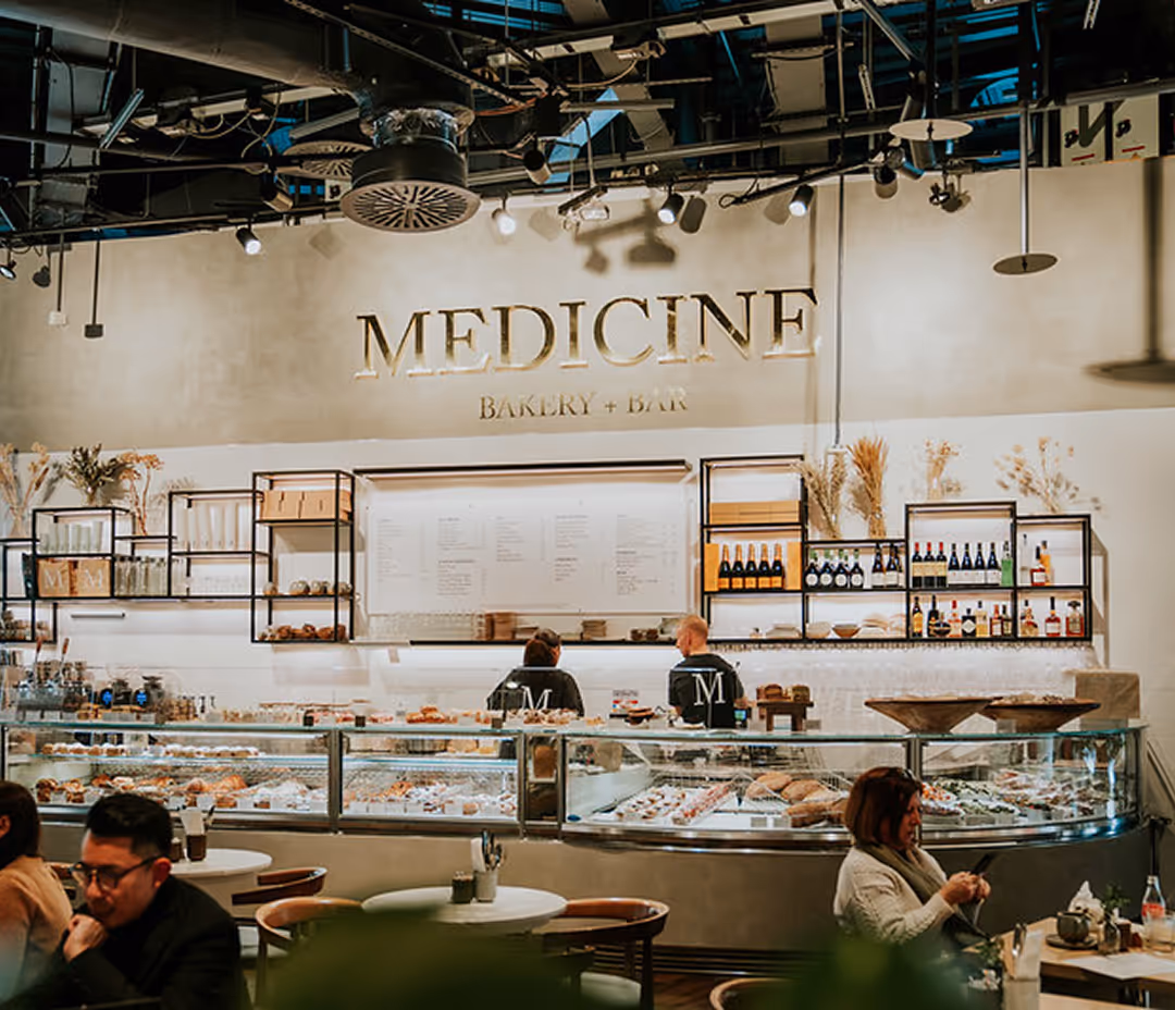 A zoomed out shot of the Medicine Bakery in Selfridges, Birmingham. Customers chat and eat in front of a counter of baked goods.