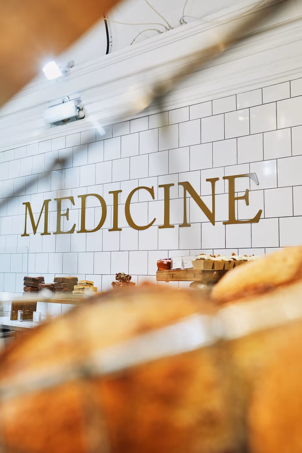 Bakery counter with various baked goods in front of a white tiled wall with the word 'MEDICINE' in large gold letters.