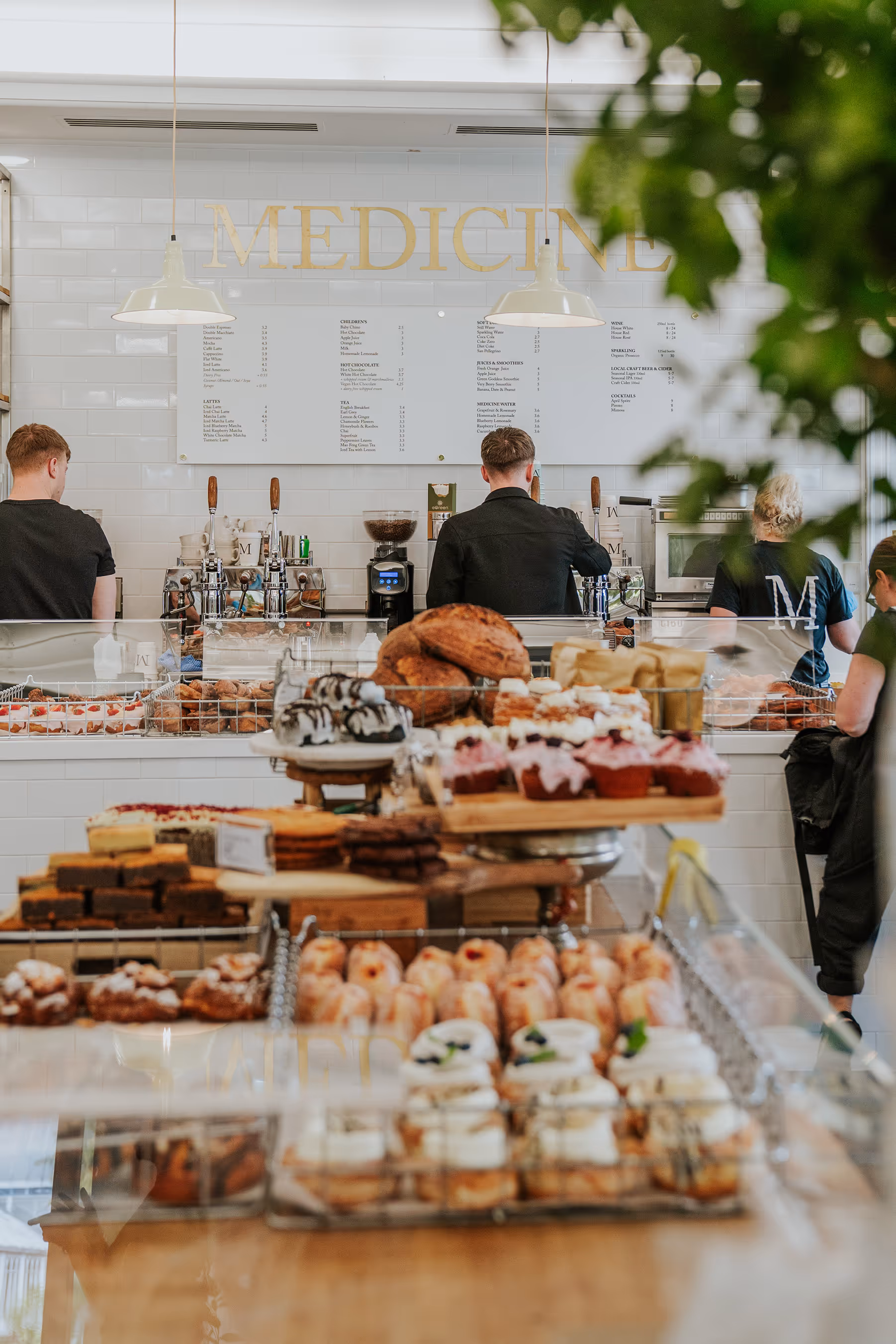 Bakery counter with assorted pastries and baked goods, with baristas working behind a white-tiled counter under hanging lights.