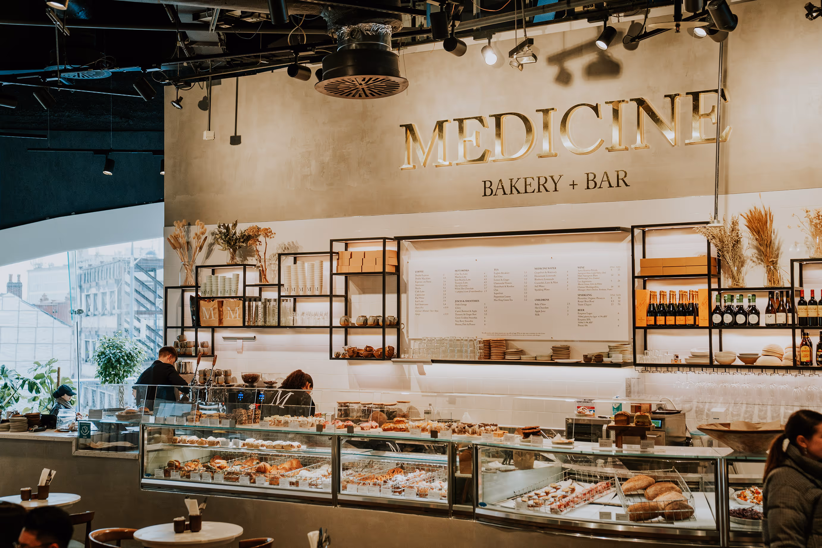 Interior of Medicine Bakery + Bar with glass display cases filled with pastries and breads and a large menu on the wall.