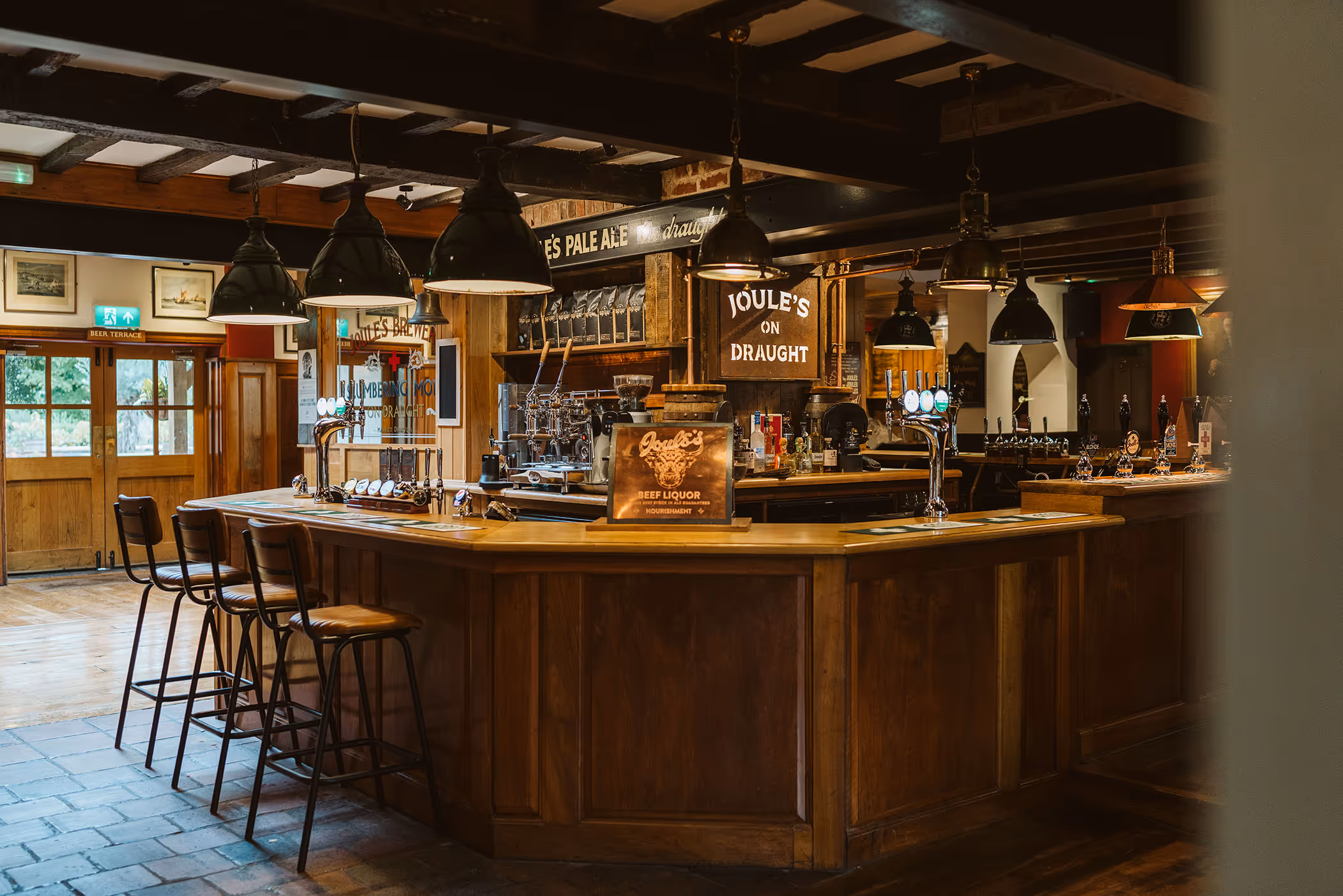 Interior of a cozy pub with a wooden bar, bar stools, hanging lamps, and beer taps.