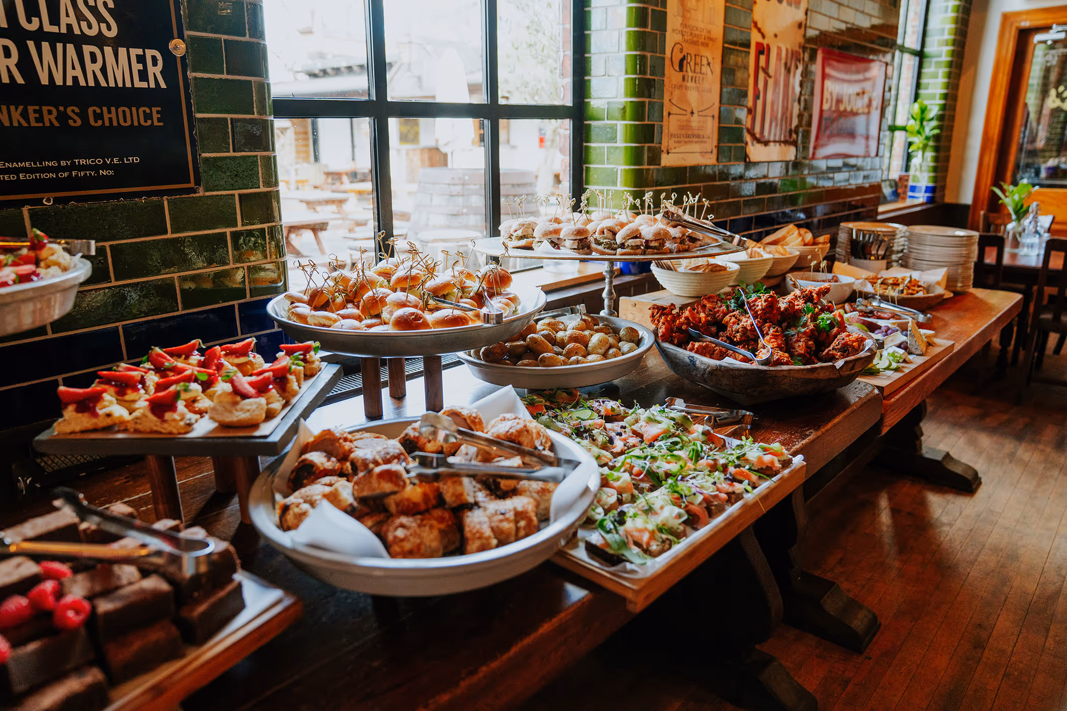 Buffet table with a variety of finger foods including sliders, savory pastries, roasted potatoes, chicken wings, and assorted appetizers in a restaurant setting.
