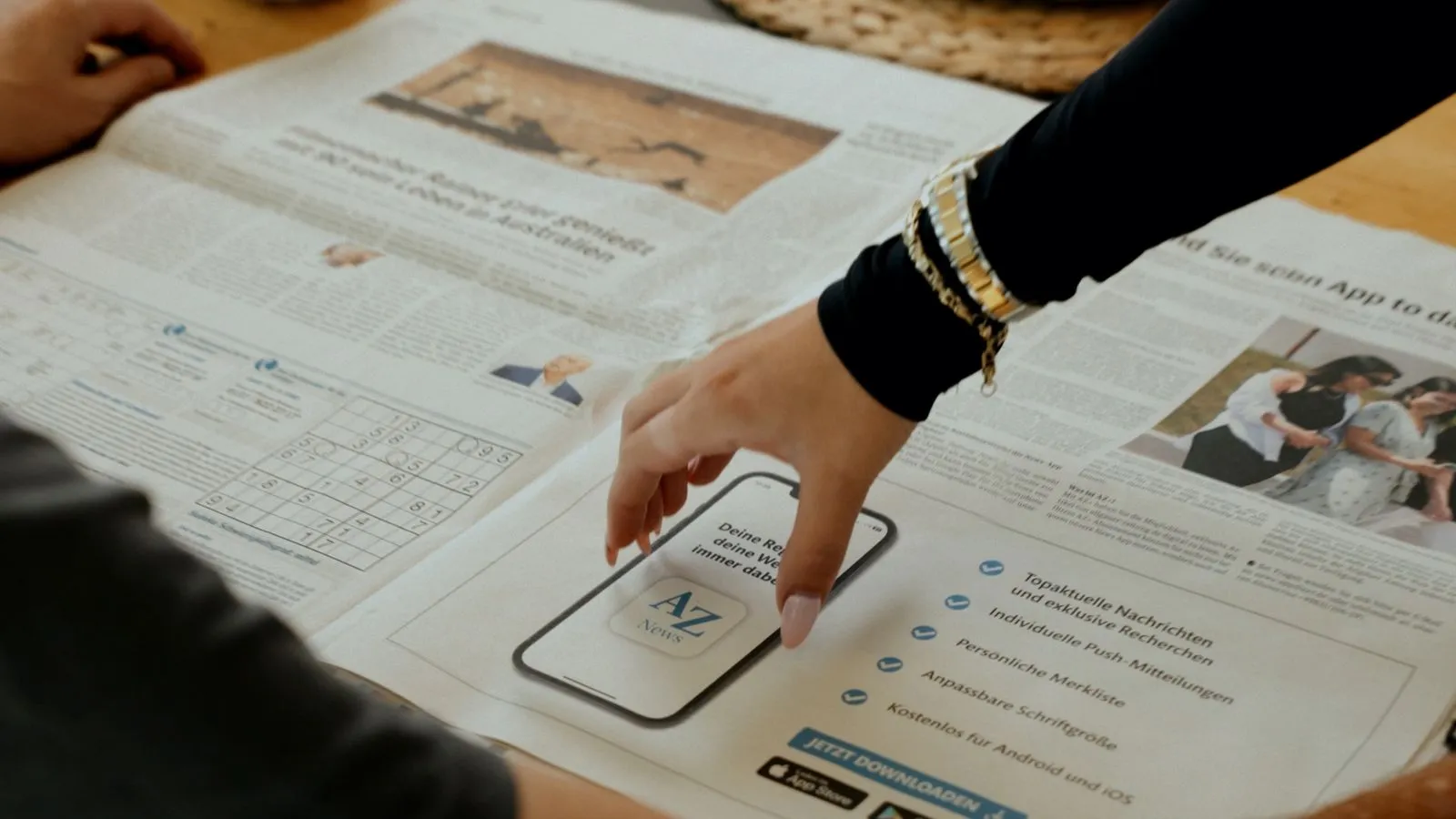 Hand tippt auf eine Smartphone-App-Anzeige in einer Zeitung mit Nachrichtenfunktionen. Foto/Video von Felix Weise, Medienproduktion für Sport, Outdoor & Events im Allgäu, Kempten und Bayern.
